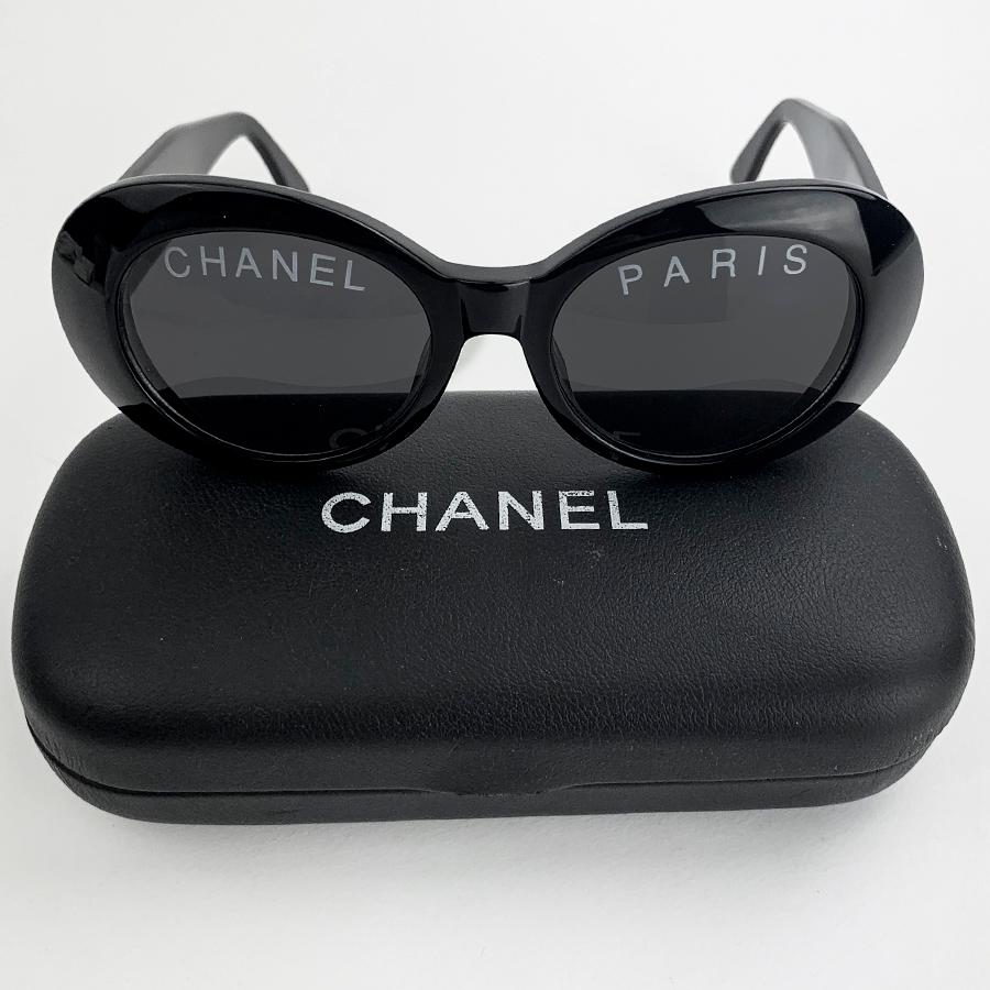 The sunglasses are from CHANEL. They are oval in shape, black in color, one glass with the inscription CHANEL, the other with the inscription PARIS. Each branch has the double C of the brand in gold metal.
The glasses are a vintage model in very
