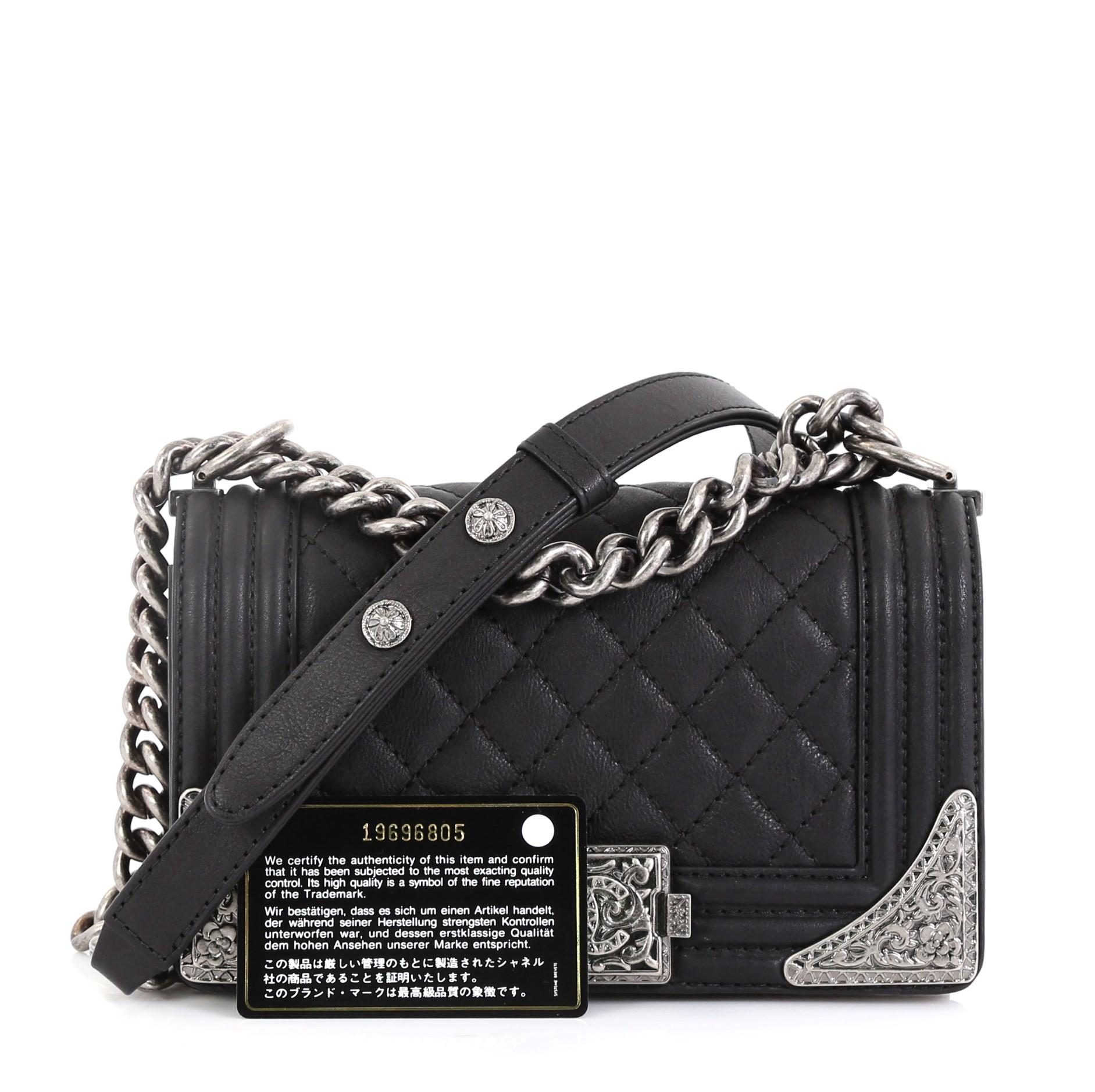This Chanel Paris-Dallas Boy Flap Bag Quilted Calfskin with Metal Adornments Small, crafted in black quilted calfskin leather, features a chunky chain-link strap with leather pad, metal adornments on both corner edges, embellished CC logo and aged