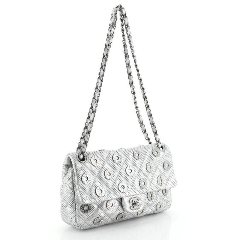 This Chanel Paris-Dubai Medals Flap Bag Quilted Embellished Perforated Leather Medium, crafted from silver perforated leather, features woven-in leather chain strap, decorative medals, and gunmetal-tone hardware. Its CC turn-lock closure opens to a