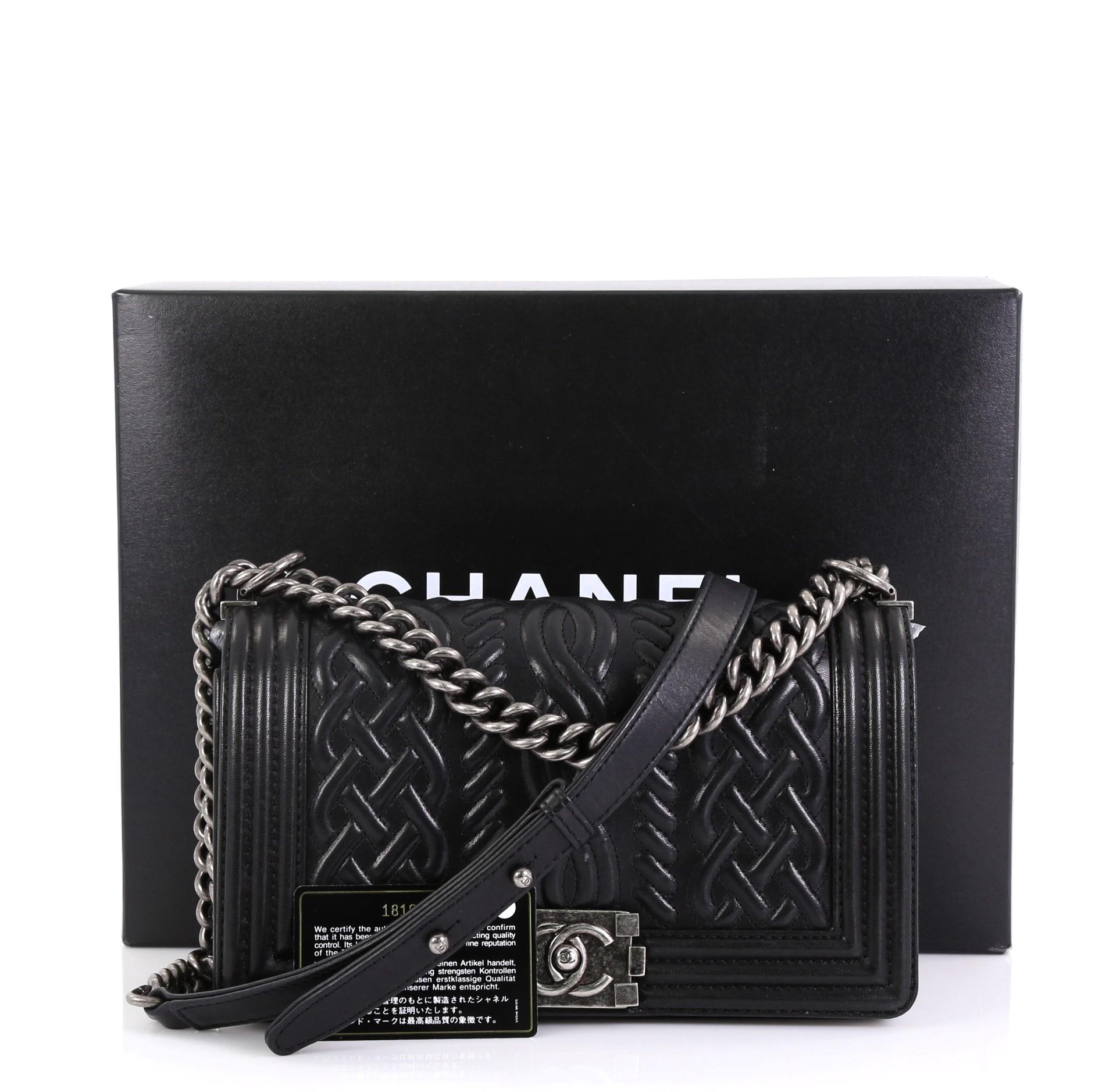 The Chanel Paris-Edinburgh Boy Flap Bag Celtic Knot Embossed Calfskin Old Medium, crafted with black celtic knot embossed calfskin, features chain link strap with leather pad and aged silver-tone hardware. Its CC Boy push-lock closure opens to a