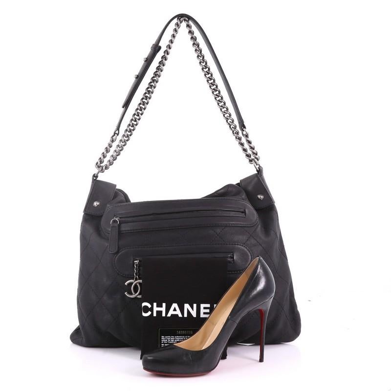 This Chanel Paris-Edinburgh Front Zip Hobo Quilted Leather Large, crafted from black quilted leather, features chain link strap with leather pad, front zip pockets, and gunmetal-tone hardware. Its snap closure opens to a black fabric interior with