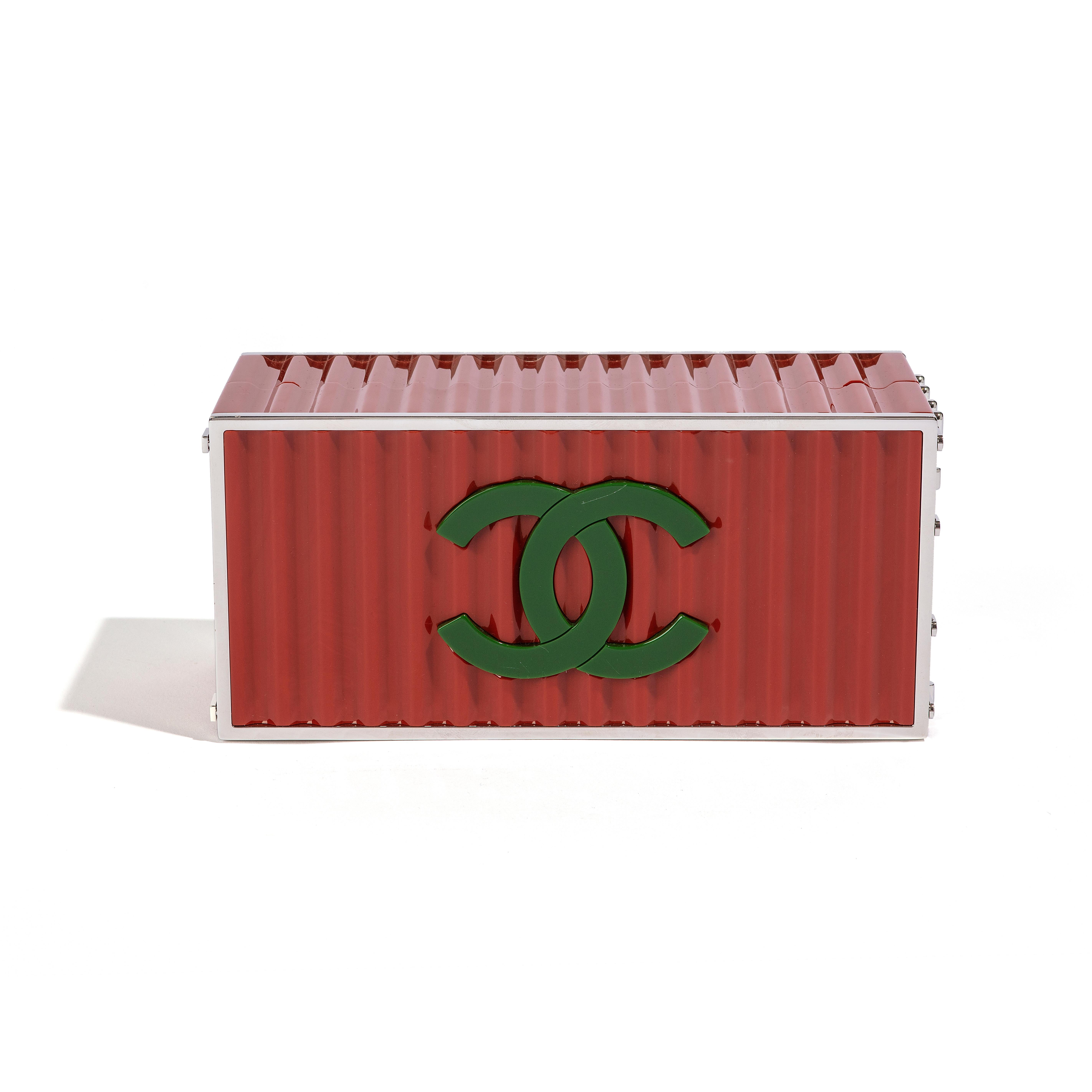 This exquisite item is a must-have for any Chanel enthusiast's collection. It is a Limited Edition Metiers D’Art 2017 Runway piece with a shipping container design. The item is made of red resin and features a chain-link strap, with the Chanel logo