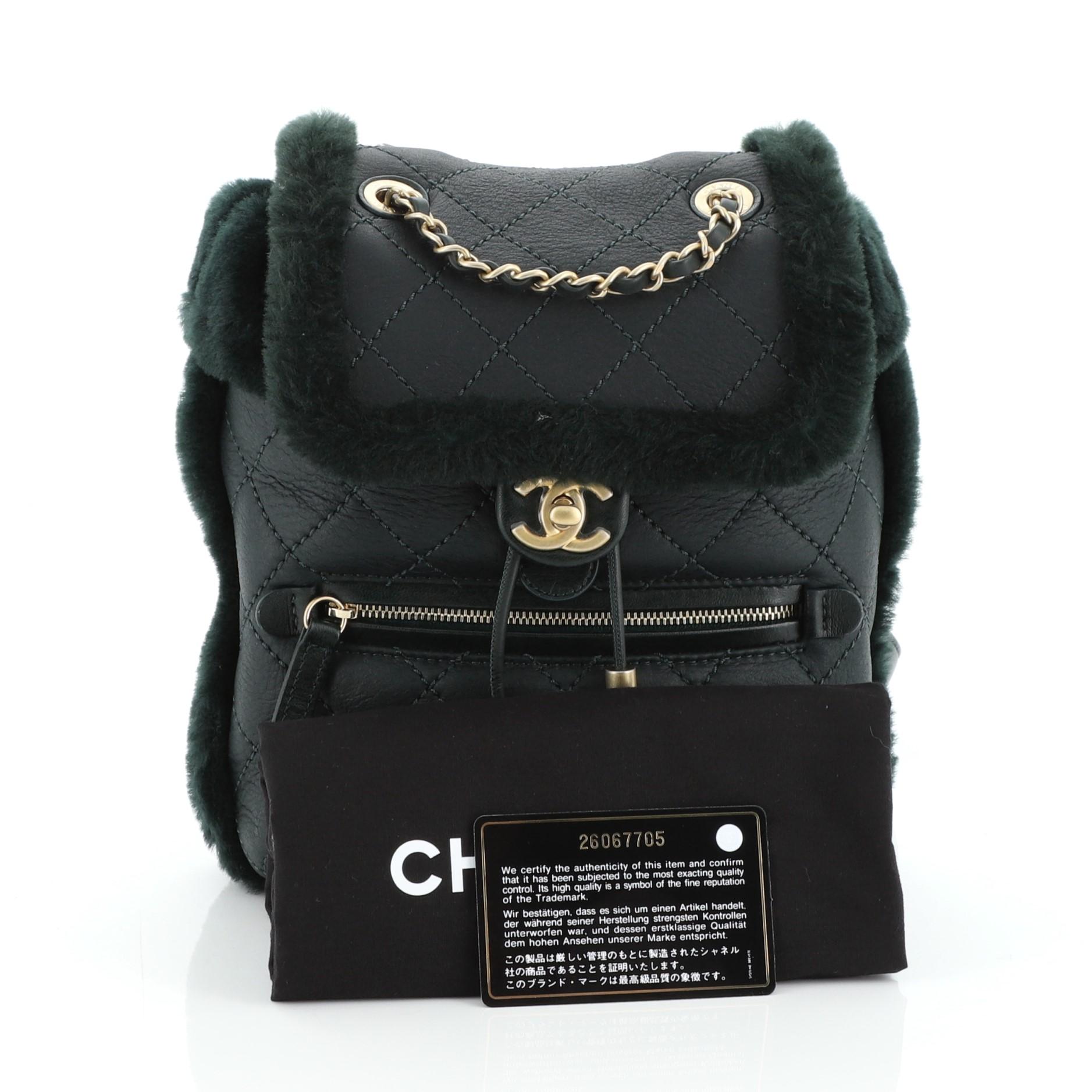 This Chanel Paris-Hamburg Flap Backpack Quilted Lambskin and Shearling, crafted in green quilted lambskin and shearling, features woven-in leather chain handle, leather straps, exterior zip pocket and gold-tone hardware. Its flap and drawstring