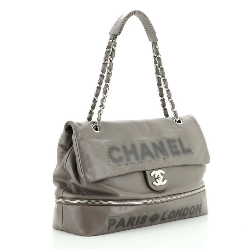 This Chanel Paris-London Expandable Flap Bag Leather Large, crafted from gray leather, features a chain link strap, Chanel logo in front and silver tone hardware. Its closure opens to a gray satin interior. Hologram sticker reads: 12353793