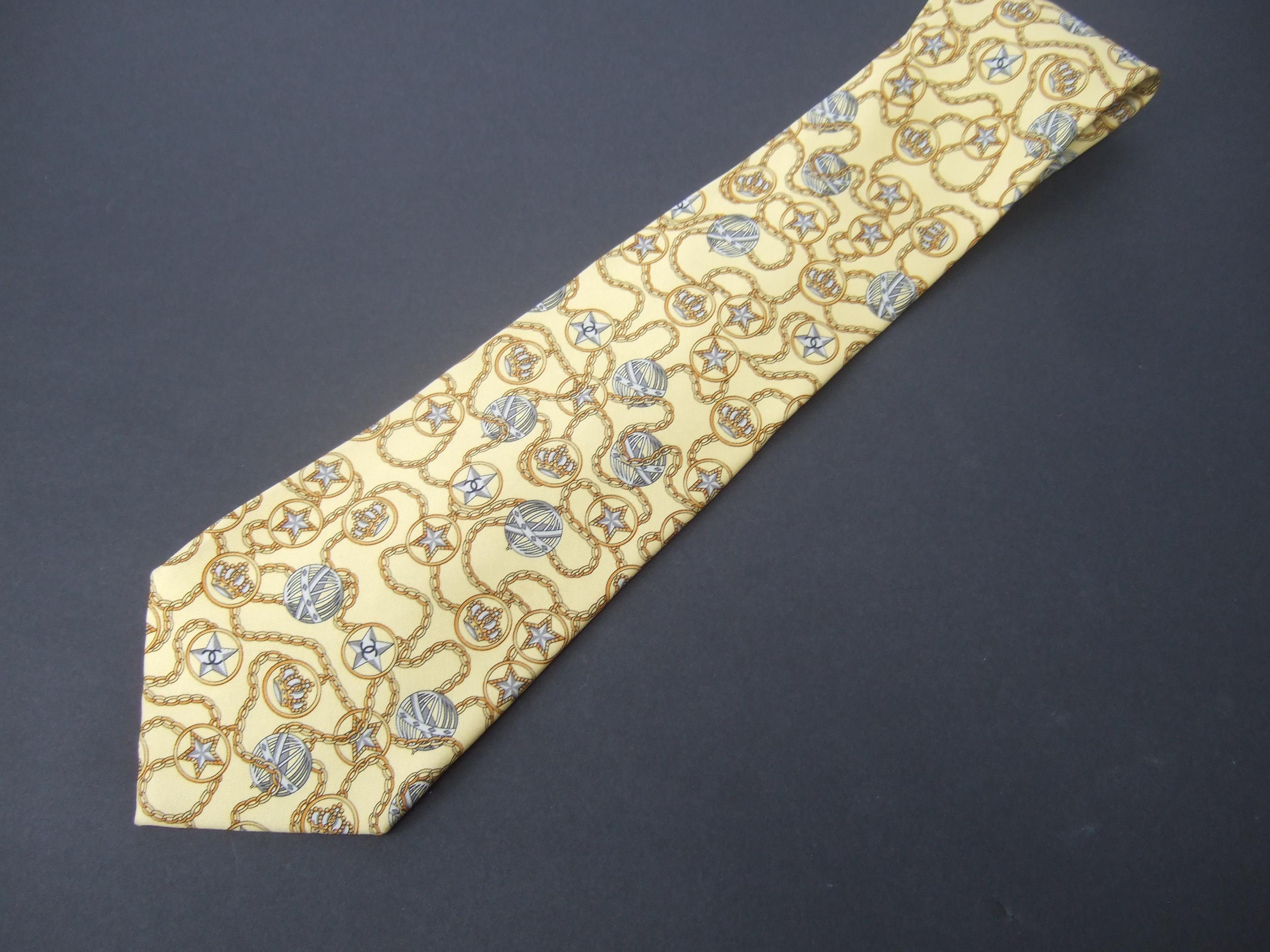 Chanel Paris Eleg stelle di seta gialle e corone  A.I.C. - Cravatte italiane anni '90 
Questa elegante cravatta di seta è disegnata con una serie di stelle grigio argento.
corone e sfere globali in tutto il mondo 

Accentuato da sinuose catene d'oro