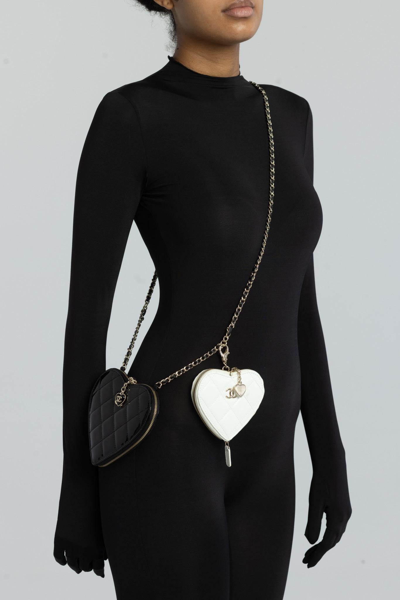These Chanel mini bags are made of patent leather in a shape of a heart in black and white. The smaller white heart is a removable pouch. The bag features a black leather threaded gold chain shoulder strap and gold Chanel CC logos. The top zip with