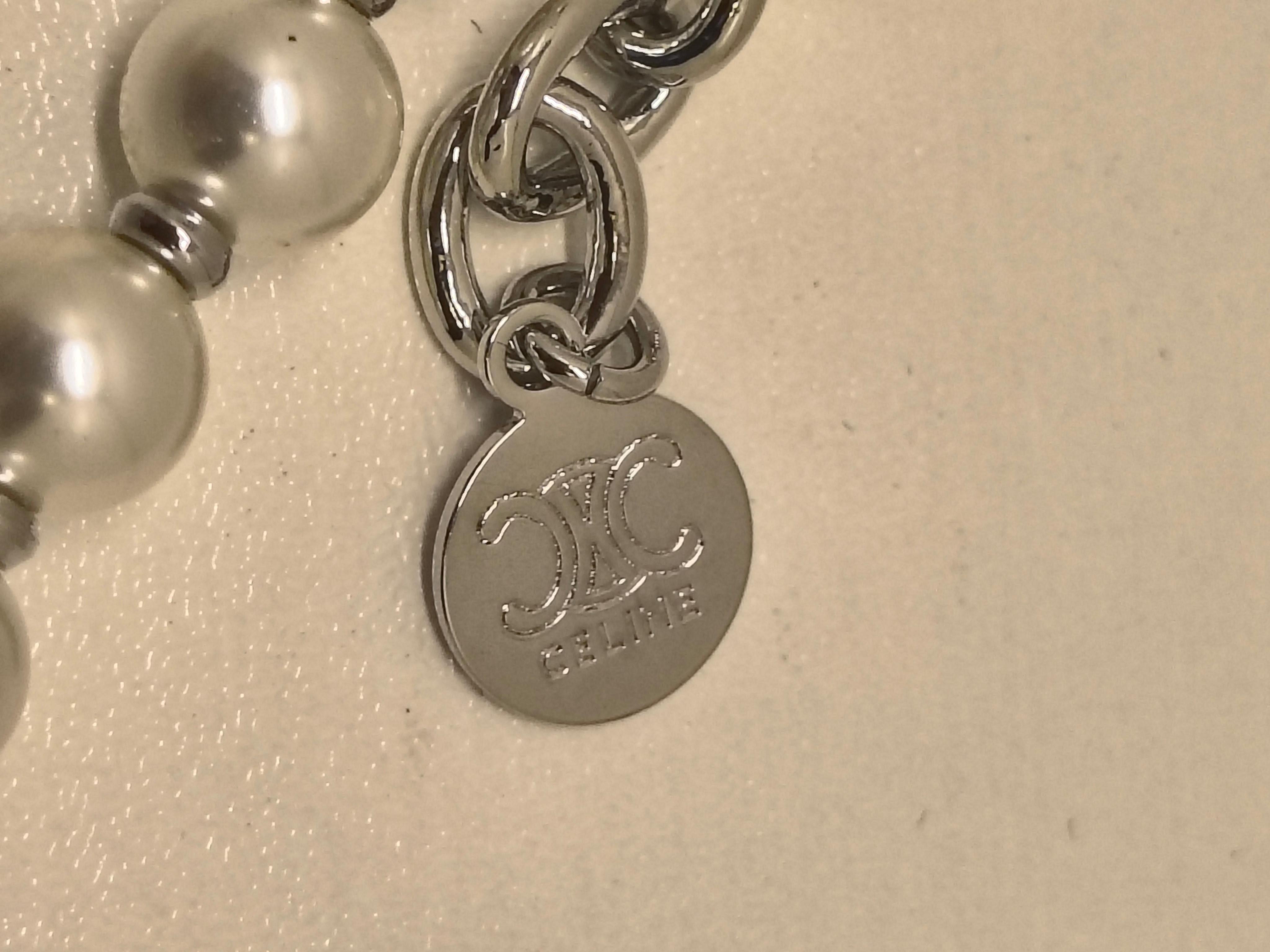 Collar de perlas Celine con logotipo Triomphe - Elegancia moderna

Este collar de perlas Celine combina la elegancia atemporal con el refinamiento parisino contemporáneo. Con una cadena de lustrosas perlas de imitación, la pieza está centrada con el