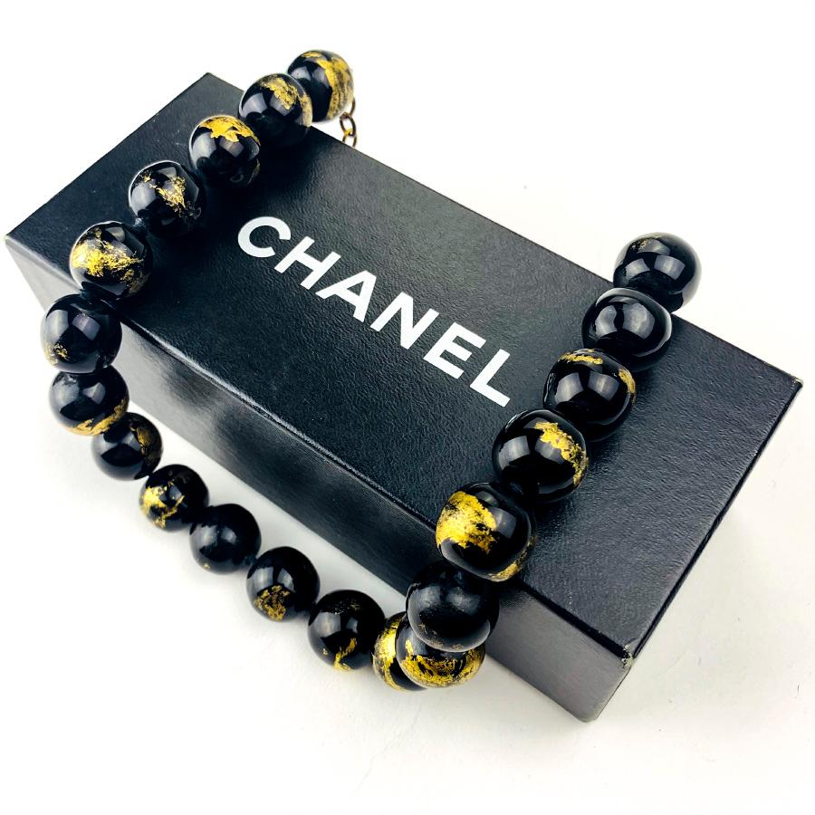 The necklace is from Maison CHANEL. It is a choker of black pearls in glass paste covered with gold leaf.
The jewel is in very good condition, the glass paste and its gold leaf are intact. The clasp is a hook that includes the CHANEL brand sticker