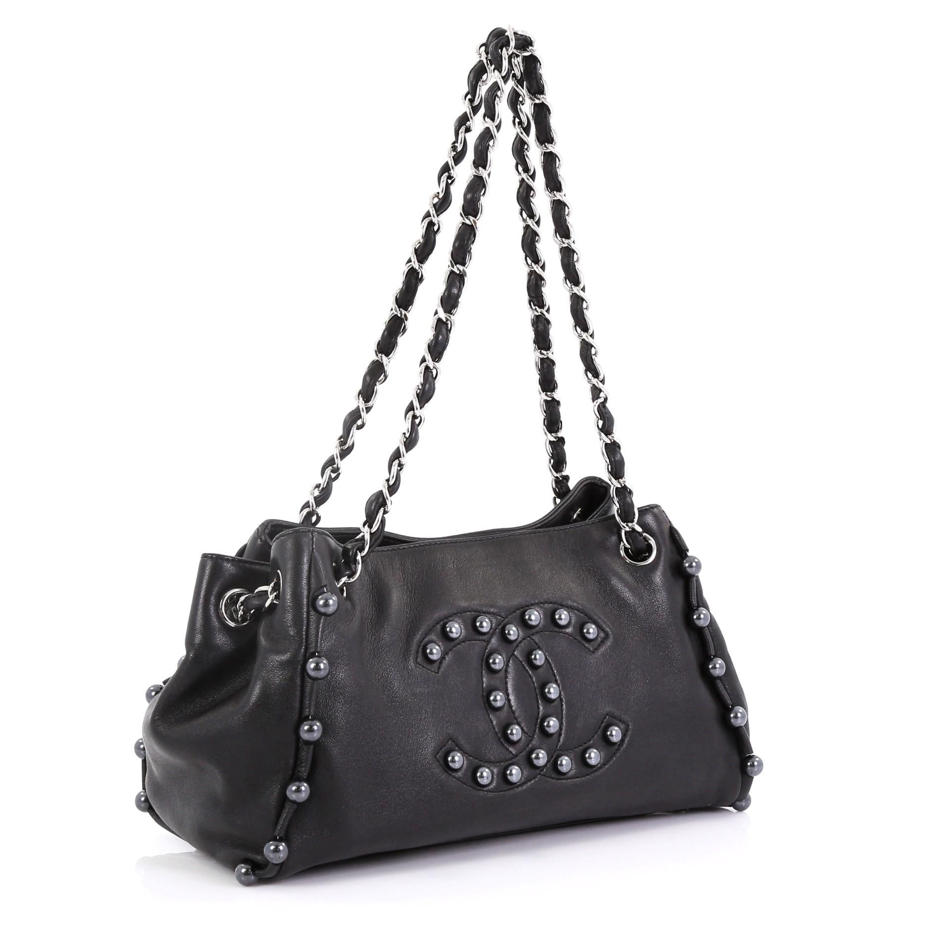 This Chanel Pearl Obsession Accordion Tote Lambskin Small, crafted from black lambskin leather, features woven-in leather chain link straps, CC logo and faux pearl trim details, protective base studs, and silver-tone hardware. Its magnetic snap