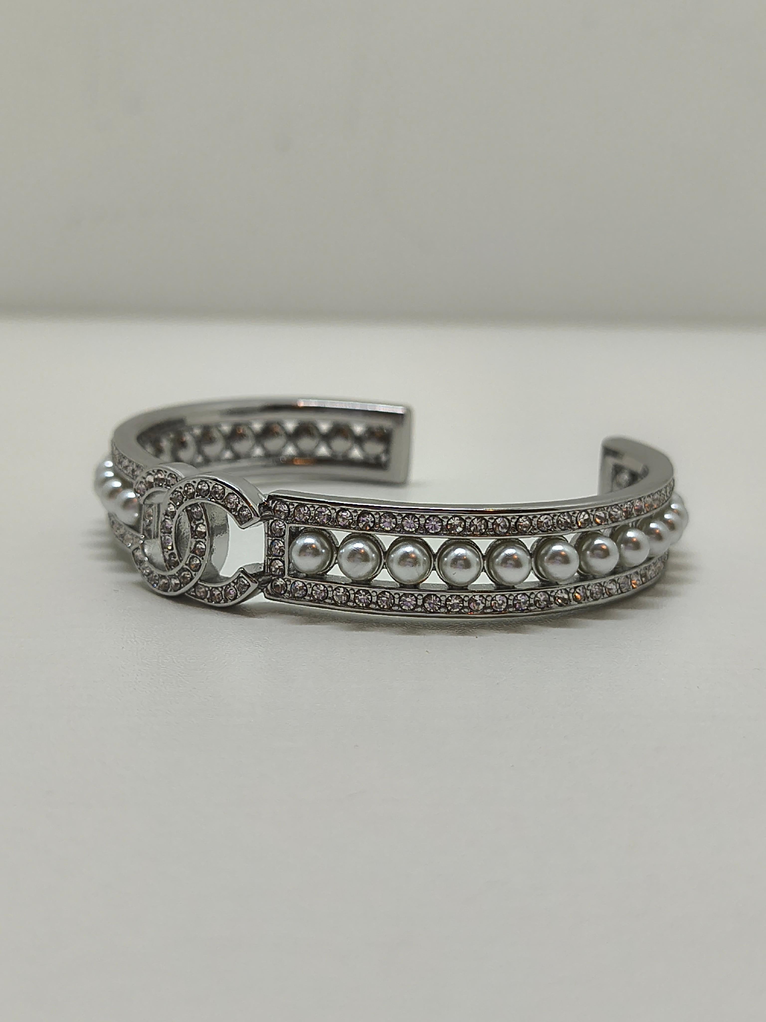 Chanel Perle & Strass CC Manschettenarmband

Dieses auffällige Chanel-Armband ist eine elegante Verschmelzung von Vintage-Look und moderner Raffinesse. Das Modell mit offener Manschettensilhouette aus antiksilberfarbenem Metall verfügt über ein