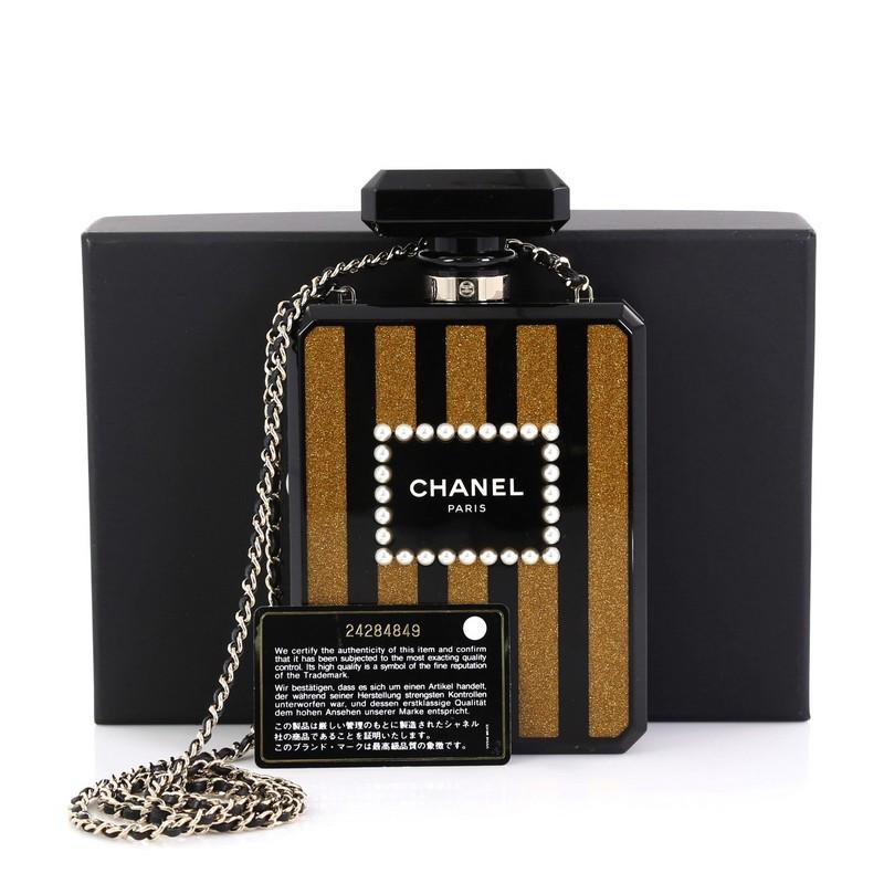 This Chanel Perfume Bottle Minaudiere Pearl Embellished Plexiglass, crafted from black and gold plexiglass, features pearl embellishments, woven-in leather chain strap, Chanel Paris logo at front, and gold-tone hardware. Its press-lock closure opens