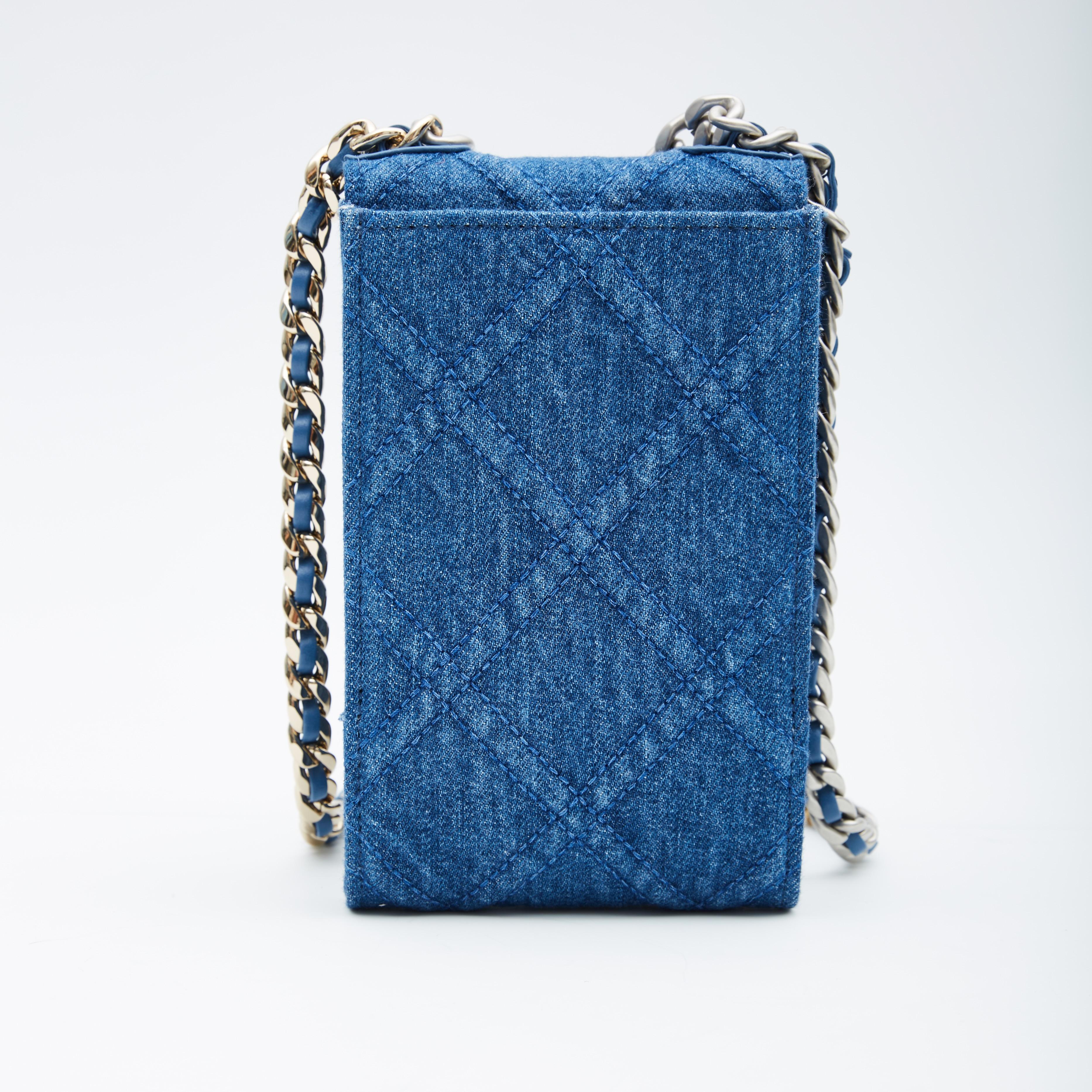 This crossbody bag is made of blue denim with blue leather details and features a sliver chain crossbody strap interlaced with blue leather, a leather shoulder pad, a front flap with snap closure, sliver tone and gold hardware and a blue fabric
