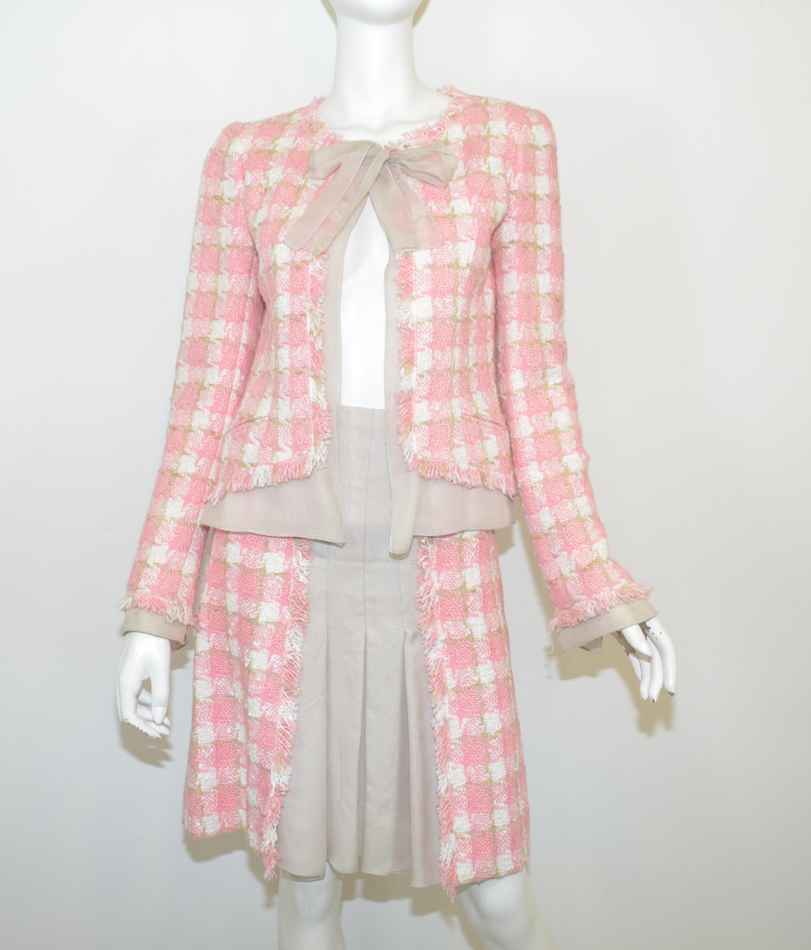 This Chanel skirt set is featured in a pink, white, and beige tweed knit with a light taupe silk chiffon trim. Jacket has a chiffon silk neck tie and button closure with two uncut pockets at the waist. Skirt has a silk chiffon pleated panel at the