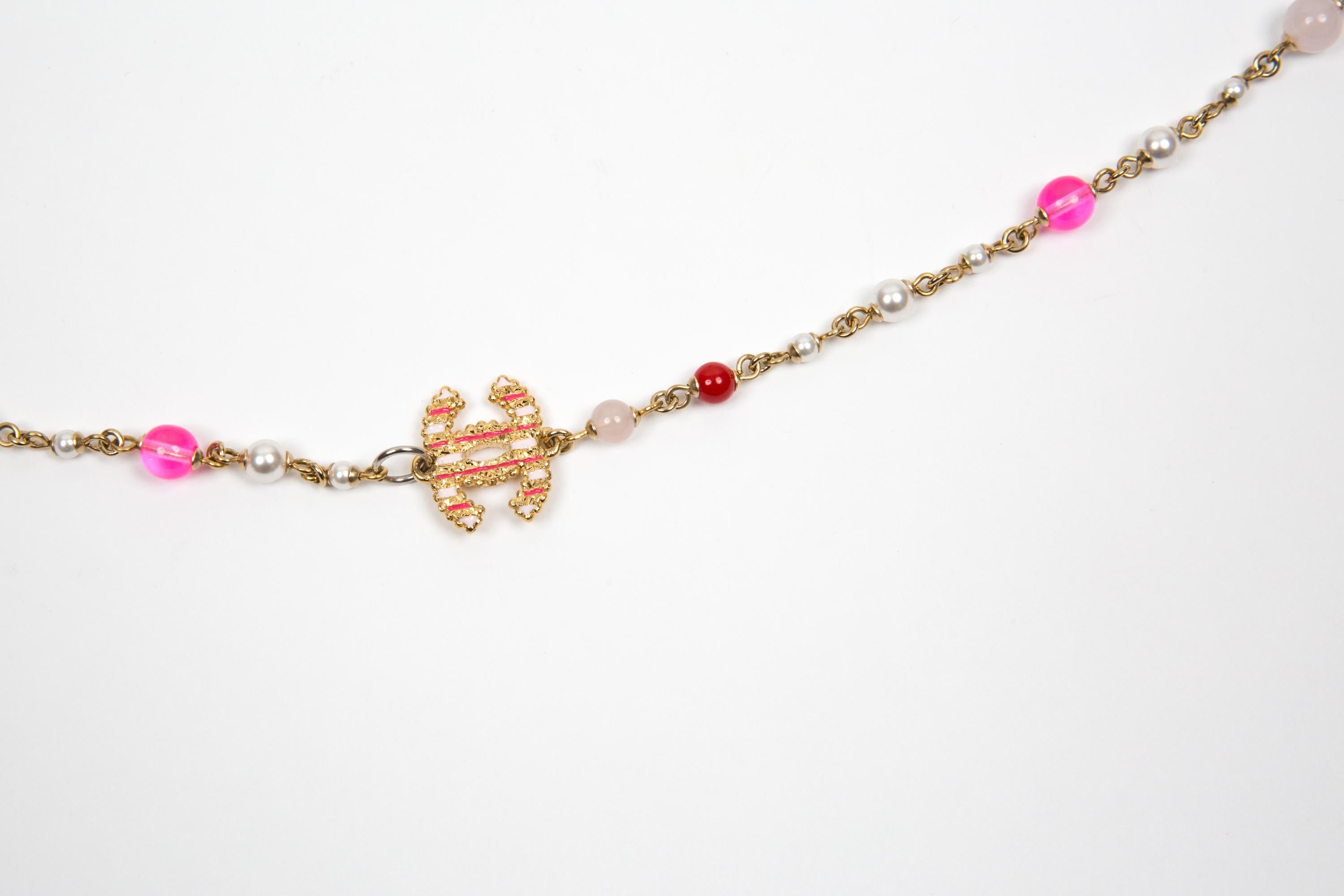 Collana sautoir impreziosita in rosa di Chanel con catena dorata, perle finte, perle impreziosite da cristalli rosa e bianchi, logo CC intrecciato, chiusura a moschettone con logo snocciolato, lunghezza regolabile con CC libera all'estremità della