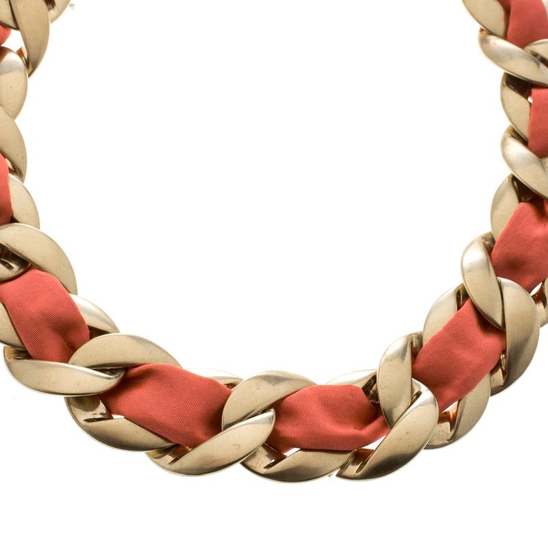 Add a truly elegant touch to your jewelry collection with this Chanel piece that personifies style in a classy way. The piece is styled as a choker and designed in a gold-tone chain link with pink fabric laced through it. It is completed with the