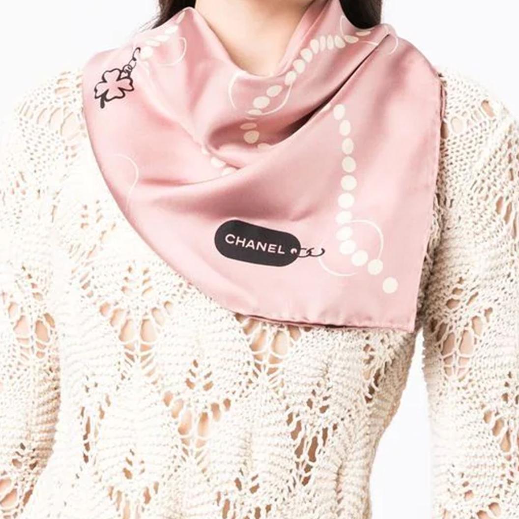 Crafted from brown silk, this pre-owned Chanel scarf features chains of pearl necklaces finished with signature Chanel motif charms such as the camellia, the number 5, and the four-leaf clover. Wear it looped around your neck or knotted in your