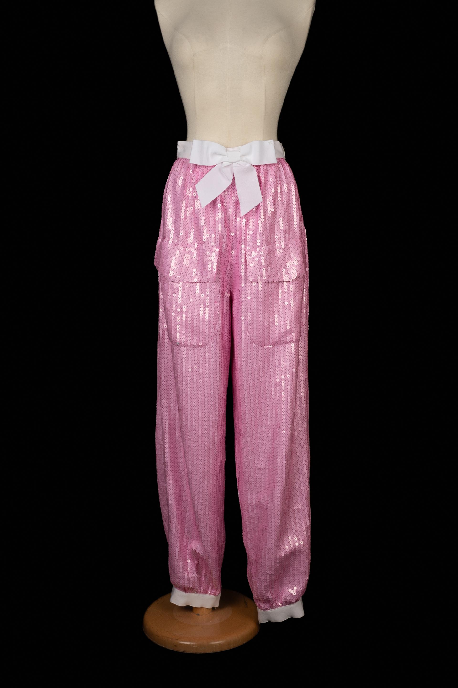 CHANEL - Pink sequined trousers with a white bow belt. No size indicated, it fits a 34FR/36FR.

Condition:
Very good condition

Dimensions:
Waist: 32 cm - Hips: 53 cm - Length: 110 cm

SKU:FJ123