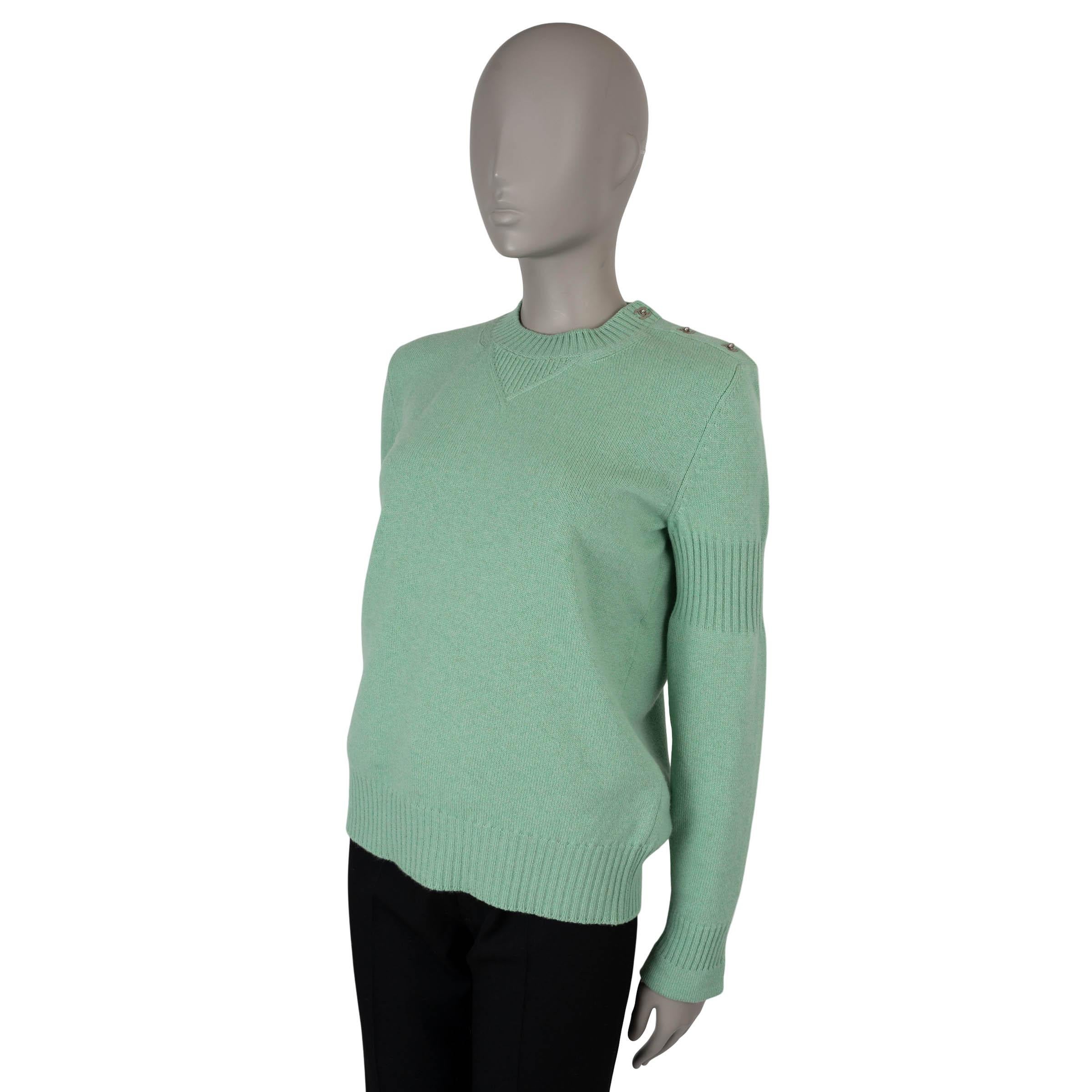 Ce pull classique 100% authentique de Chanel est confectionné en cachemire doux vert pistache (100%). Il présente d'élégantes attaches CC argentées au niveau du cou, ainsi qu'un col ras du cou, des finitions en tricot côtelé et des détails raffinés