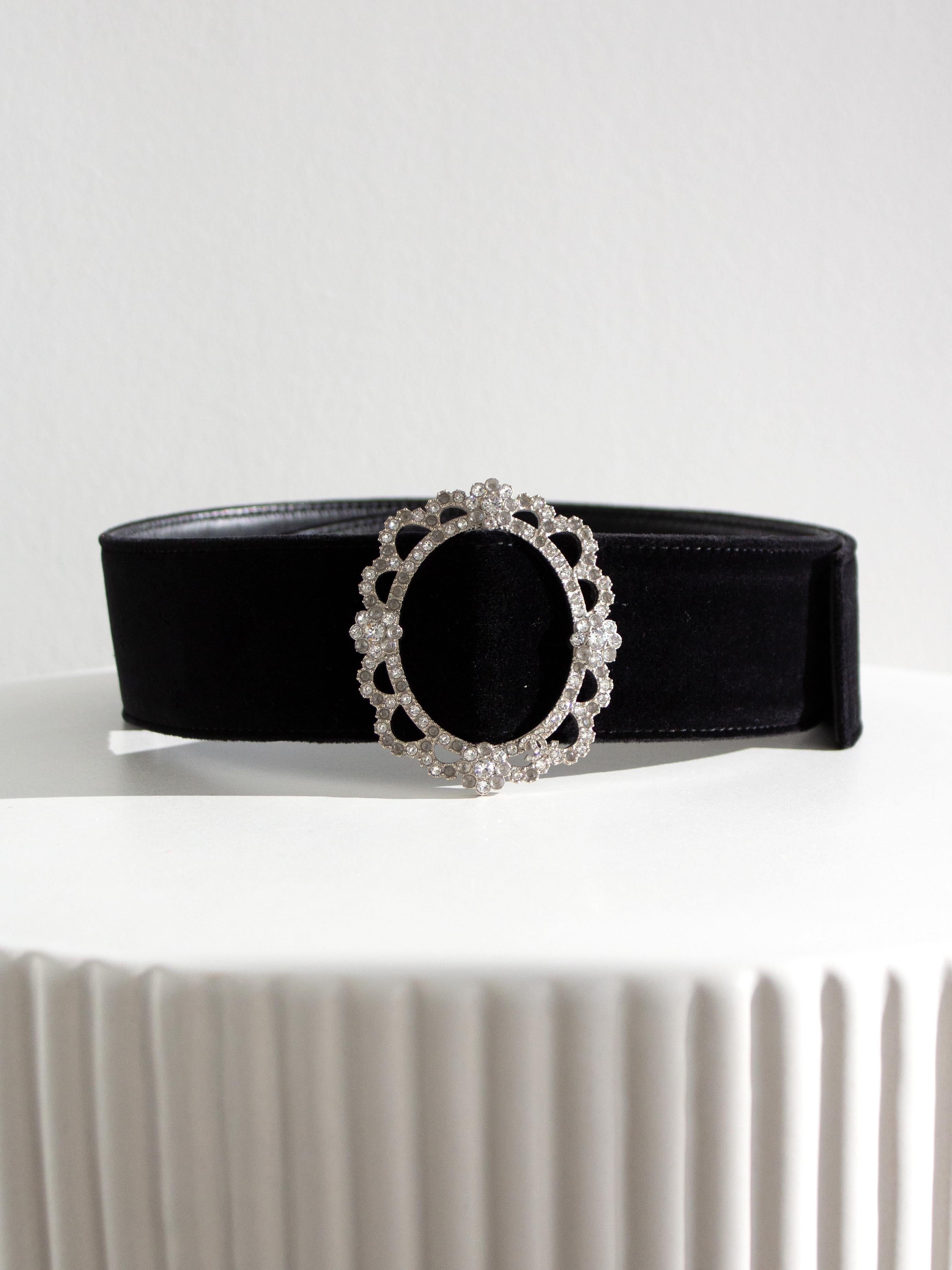 This Chanel black velvet belt is from the Pre-Fall 2015 Salzburg collection, a luxurious piece that combines elegance with a statement-making style. Crafted from plush black velvet, it features a stunning silver-tone buckle adorned with crystal