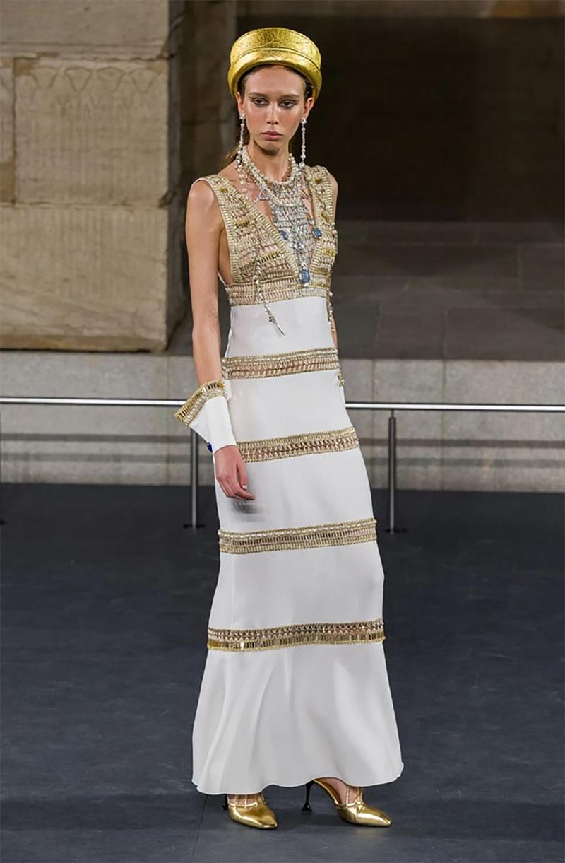 CHANEL

The Chanel dress from the Pre-Fall Egyptian 2019 collection is made of white fabric.
 Decorated with golden inserts and pearls.
 Straight silhouette, sleeveless, back zip fastening. 
Cuffs included. Without lining.


France, 2019.

Content: 