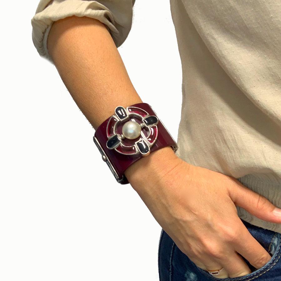 This CHANEL cuff in purple plexiglass is embellished with a piece of gold metal set with purple resin and a pearl in the center. The jewelry is silver metal.
This CHANEL bracelet is in very good condition. The mother-of-pearl is slightly chipped.
