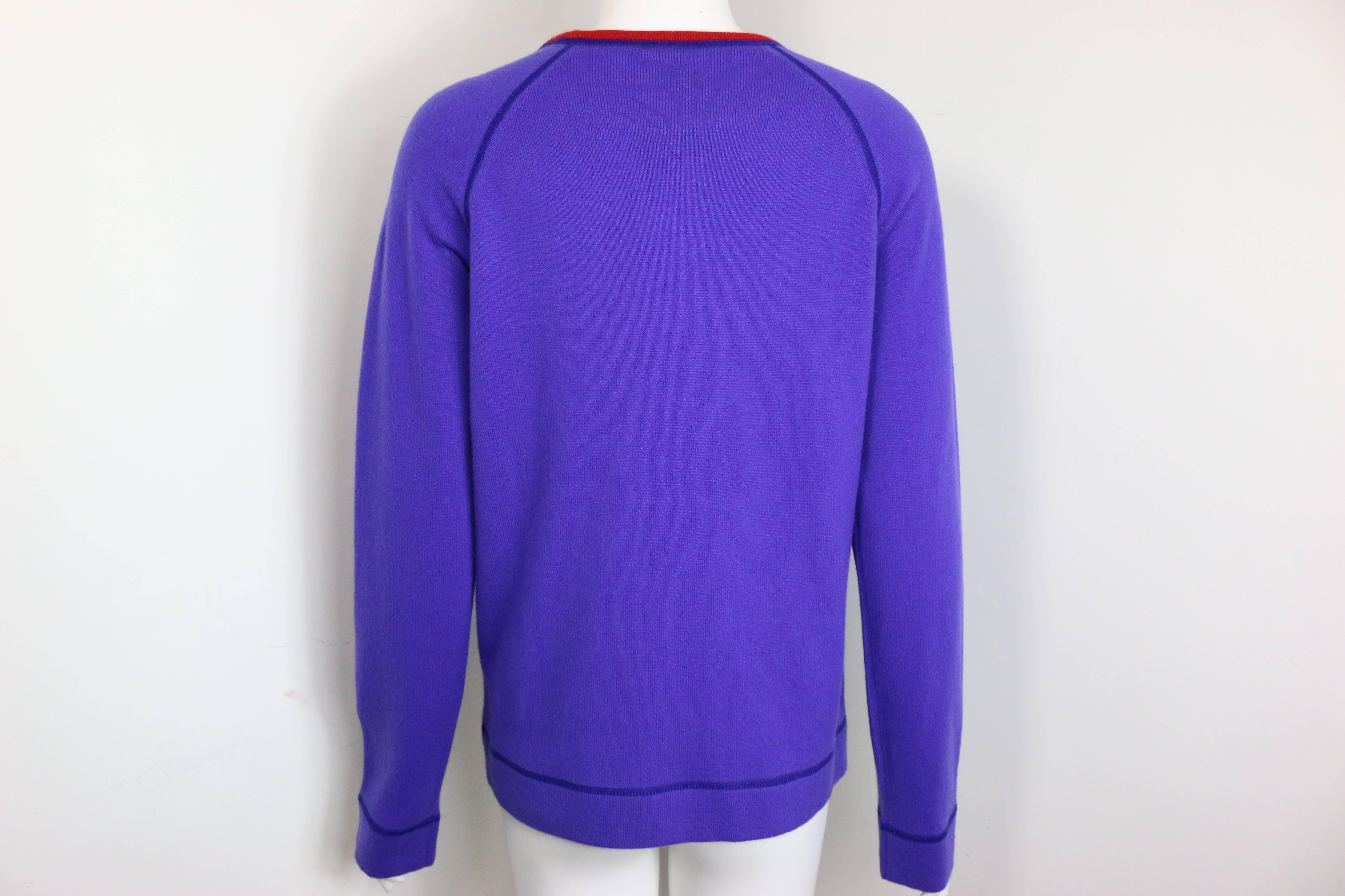 - Pull-over en cachemire violet à col bordé de rouge de la collection 2008 de Chanel. 

- Il comporte deux poches latérales, des manches rondes et le logo 