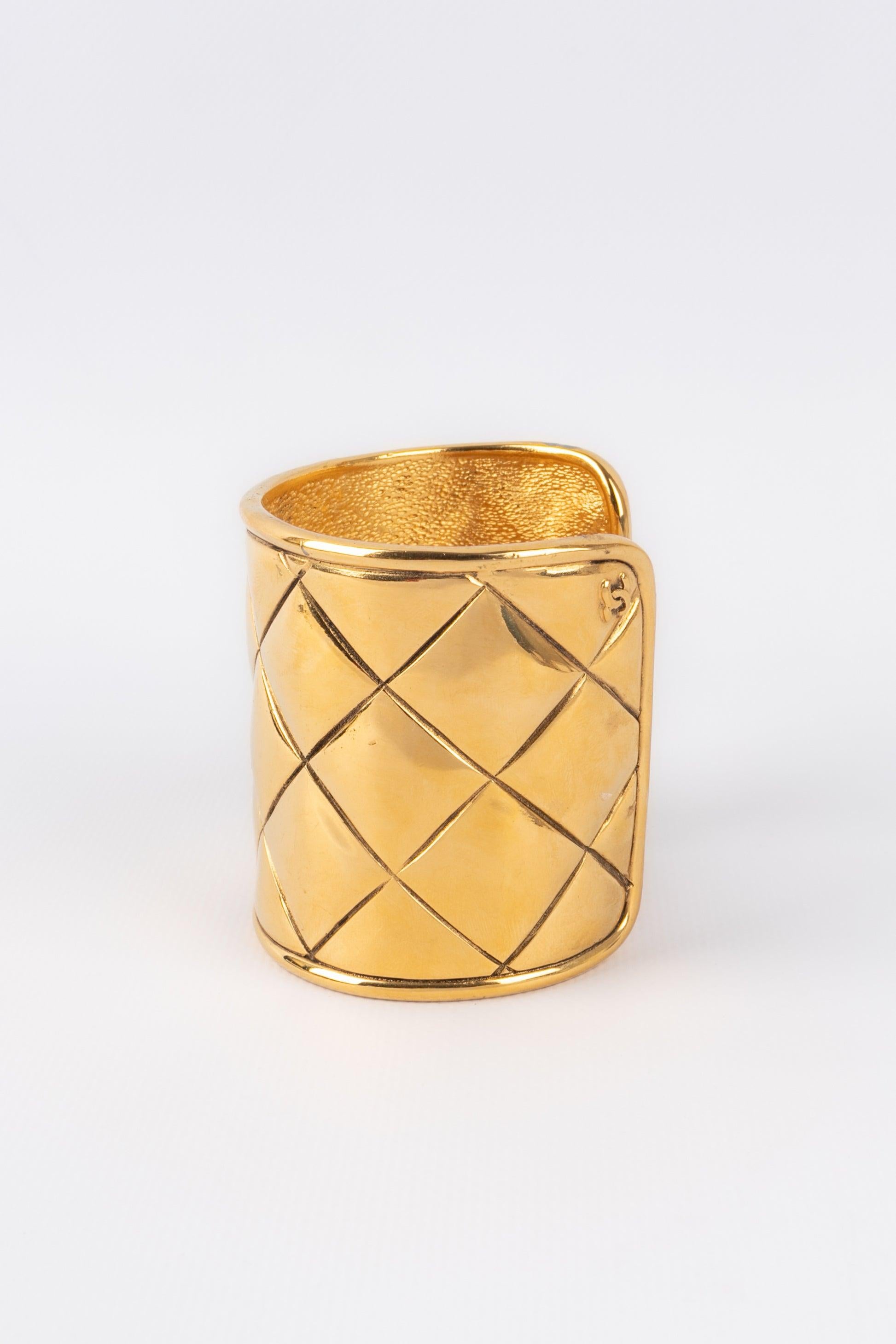 Chanel - (Fabriqué en France) Bracelet manchette en métal doré matelassé. A signaler, une petite zone de manque d'or sur le bas de la manchette.

Informations complémentaires :
Condit : Bon état
Dimensions : Hauteur : 6,5 cm - Longueur : 15 cm -