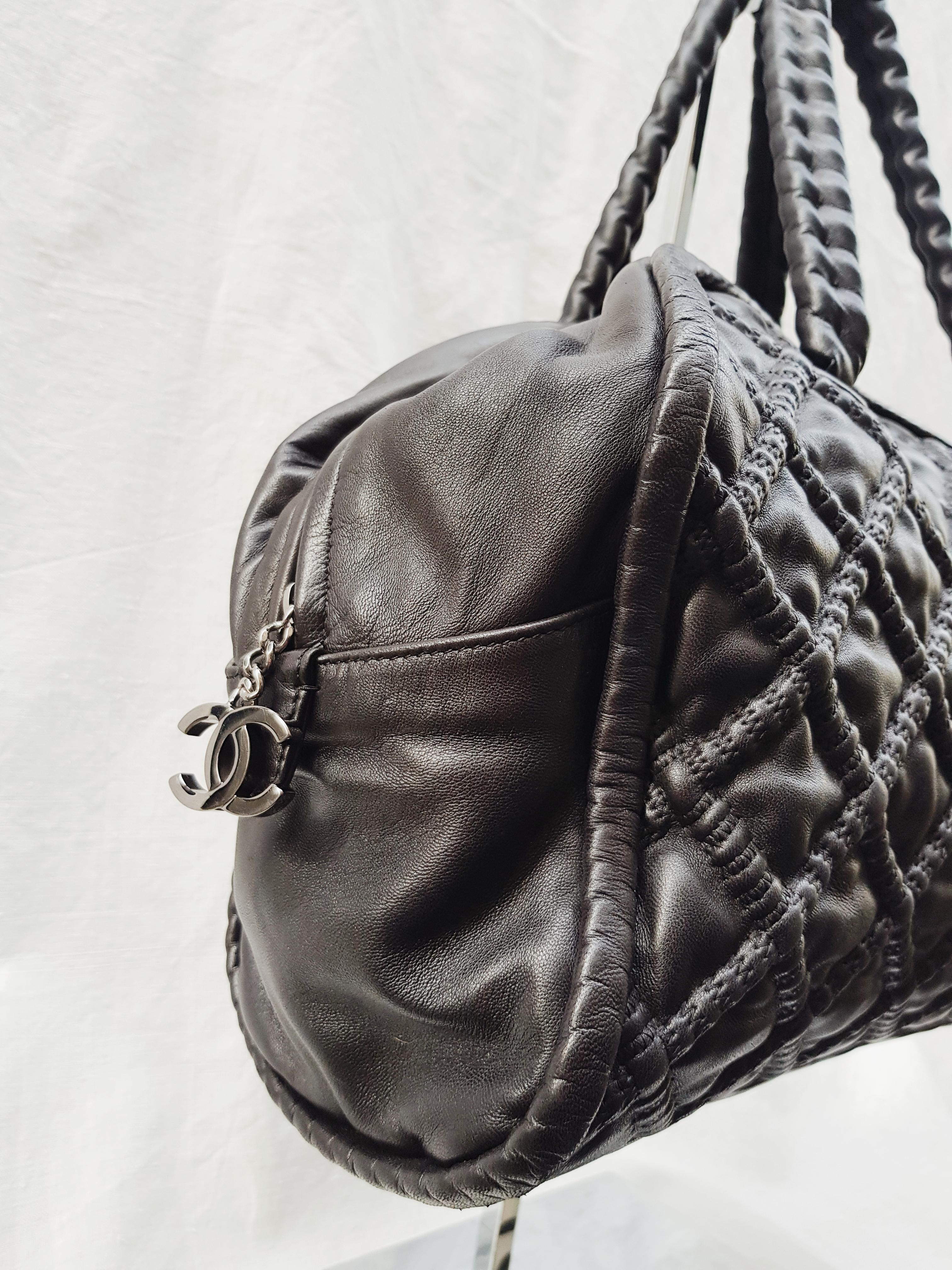This fantastic Chanel bowler bag is crafted from black quilted lambskin leather, featuring dual-hidden chain leather handles, CC charm zipper pull, and silver-tone hardware accents. Its zip closure opens to a black satin-lined interior with zip