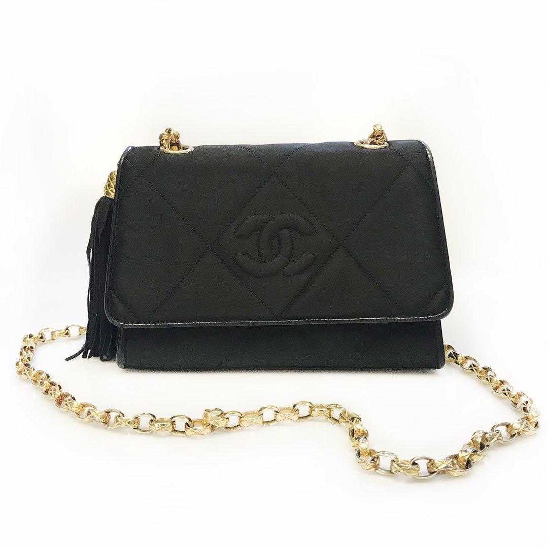 Vintage satin quilted shoulder bag by Chanel
Circa 1991-1994
Black quilted satin
CC stitched on front 
Gold tone hardware
All-metal chain shoulder strap 
Snap closure 
Decorative side tassel
Red leather interior
Zip pocket inside
Chanel stamp and