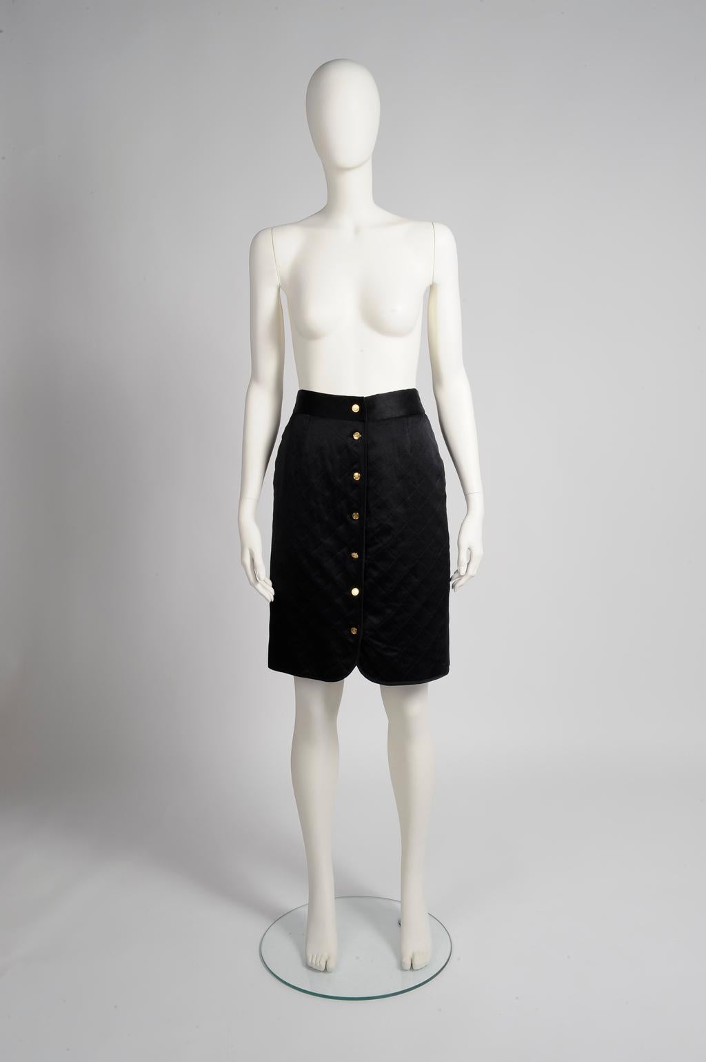 Cut in a classic pencil silhouette, this late 80's Chanel black satin silk skirt is expertly quilted to create texture and little dimension. Fully lined in black silk, it fastens down the front with seven gilt metal buttons with Chanel bag 