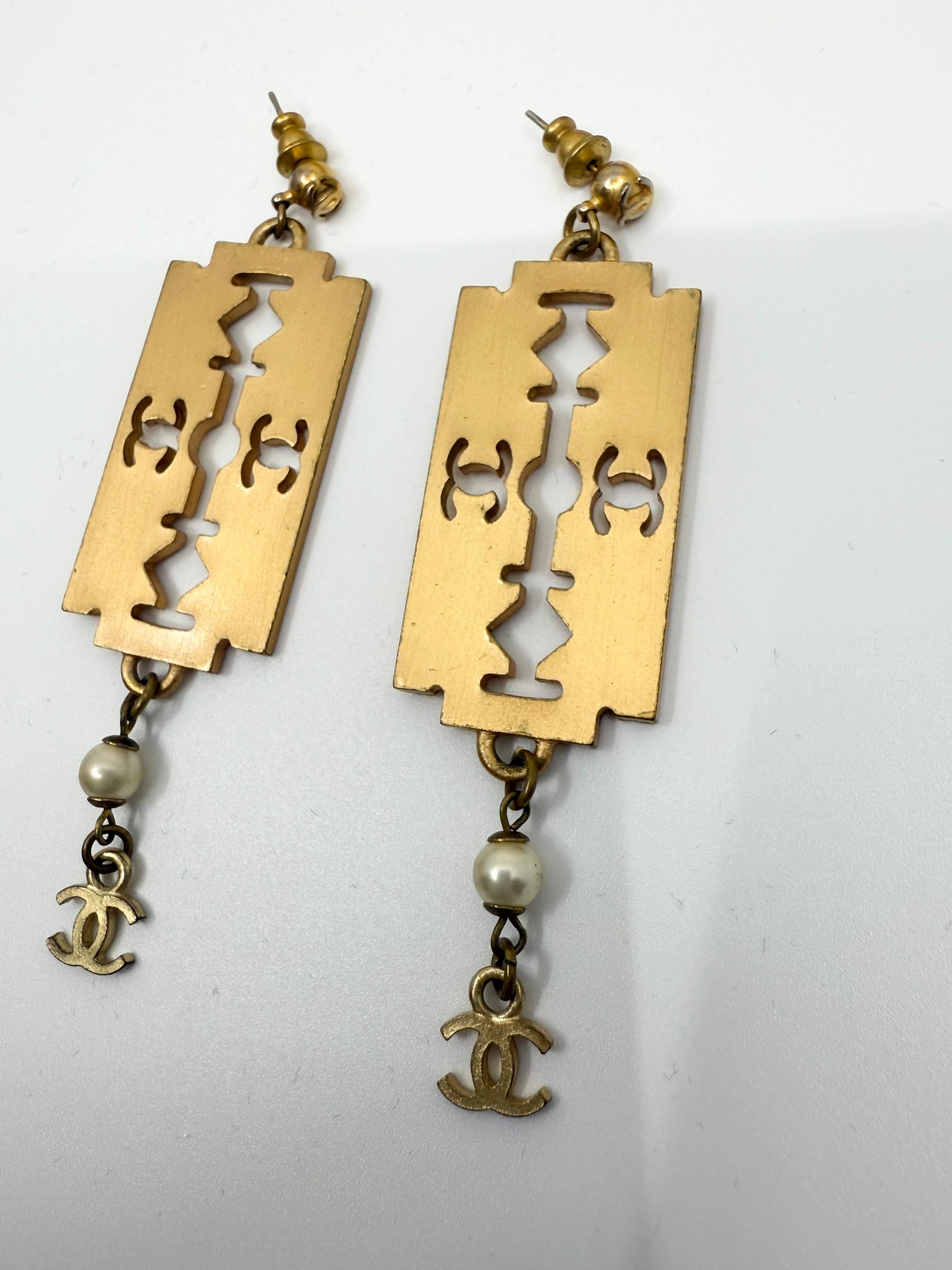 Uno dei design più audaci e provocatori mai realizzati da Chanel, questi orecchini da passerella del 2001 sono un raro tesoro da collezione. Modellate come lame di rasoio, le piastre rettangolari in tonalità oro sono trafitte da loghi CC in