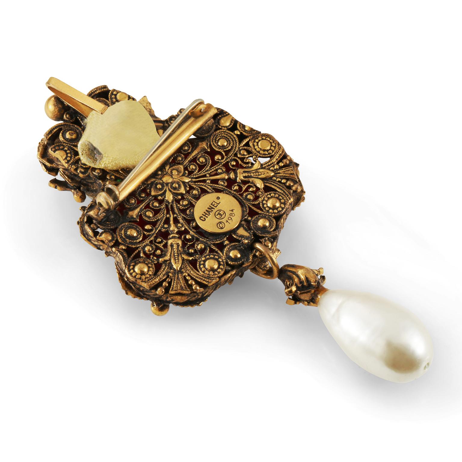 This authentic Chanel Gripoix and Pearl Baroque Brooch is in beautiful vintage condition from the 1984 collection.  Large red and green emerald cut Gripoix glass stones have ornate gold surround.  A faux teardrop pearl dangles from the bottom. 
