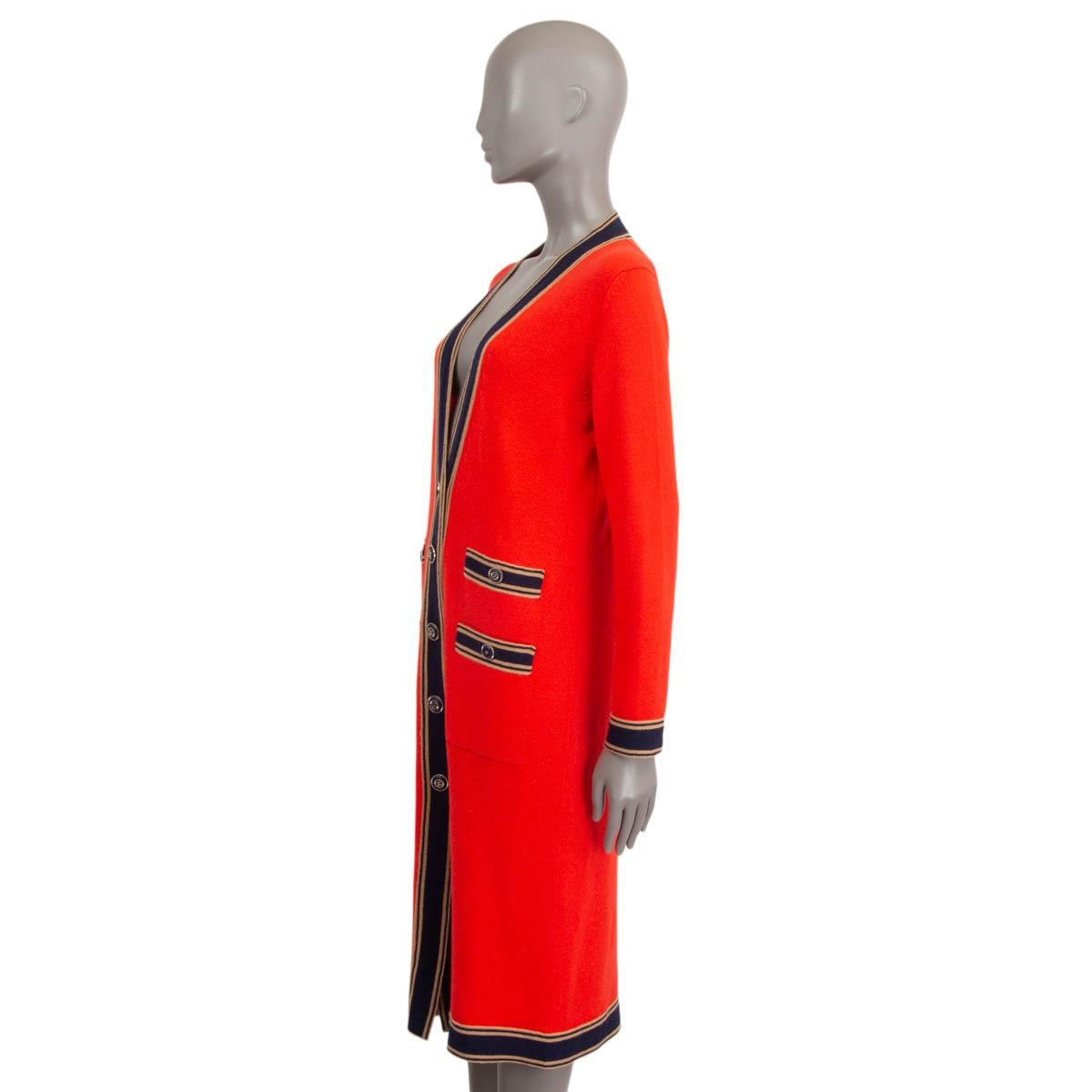 This 100% authentic Chanel long cardigan in red cashmere combines timeless elegance with a touch of classic contrast. It features a deep V-neck, accented by black and camel striped trims, and four buttoned patch pockets for added style and