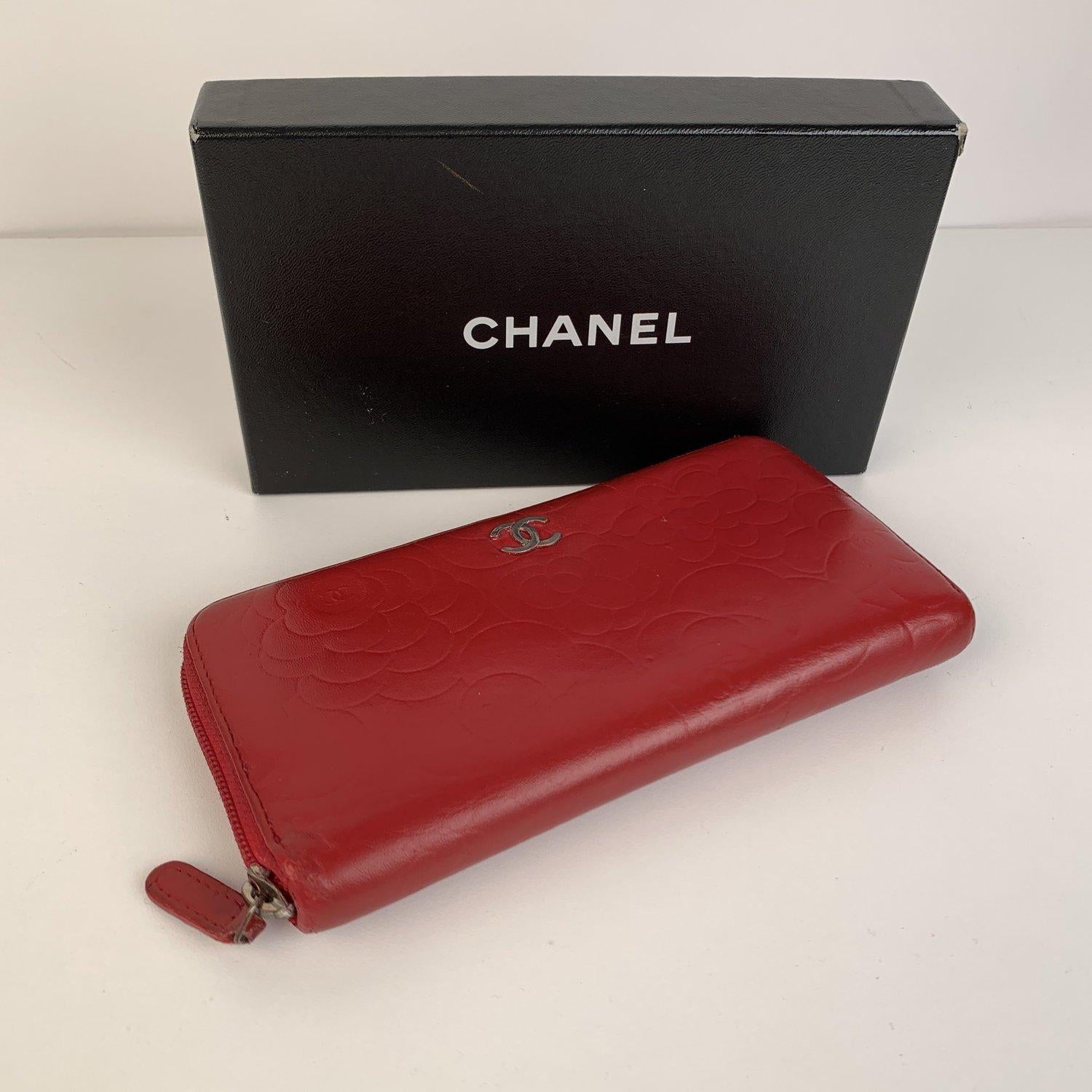 Chanel embossed Zip Around Wallet, crafted from red embossed leather with camellia flower design. Silver metal CC - CHANEL logo on the front. Zip-around closure. Pink/Purple leather interior. Inside it has 8 credit card slot, 2 open pockets, 1 zip