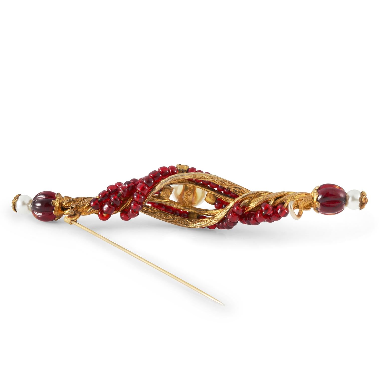 This authentic Chanel Red Gripoix Bead and Pearl Pin is an early vintage piece in excellent condition.  Gold twisted design incorporates red Gripoix beads and a center faux pearl flanked by four small crystals.  Finial capped ends each have a small
