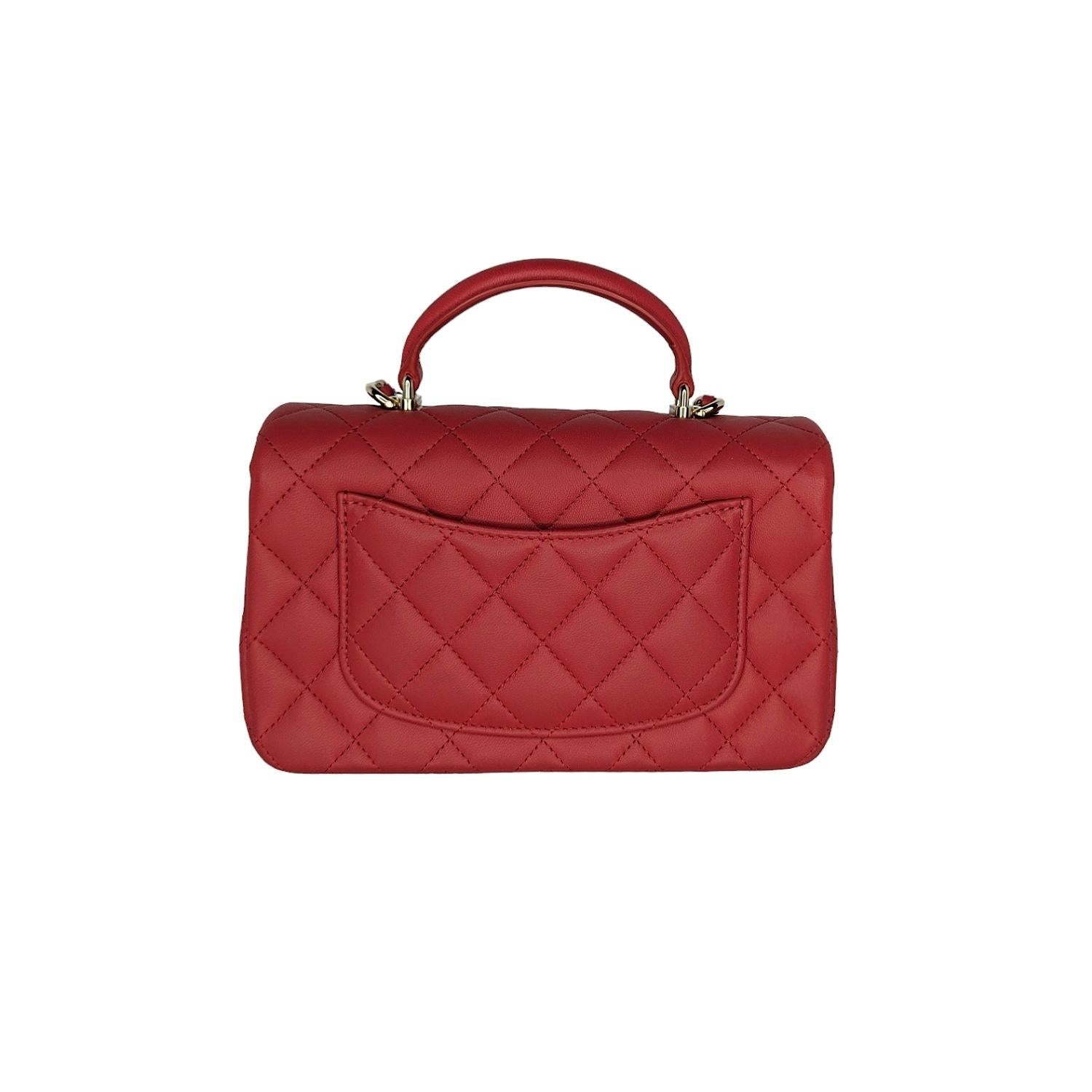This stunning Chanel mini flap top handle bag is a timeless and chic accessory that is perfect for any occasion. The bag is crafted from luxurious lambskin leather in a beautiful red color. The bag features a leather top handle, a gold chain link