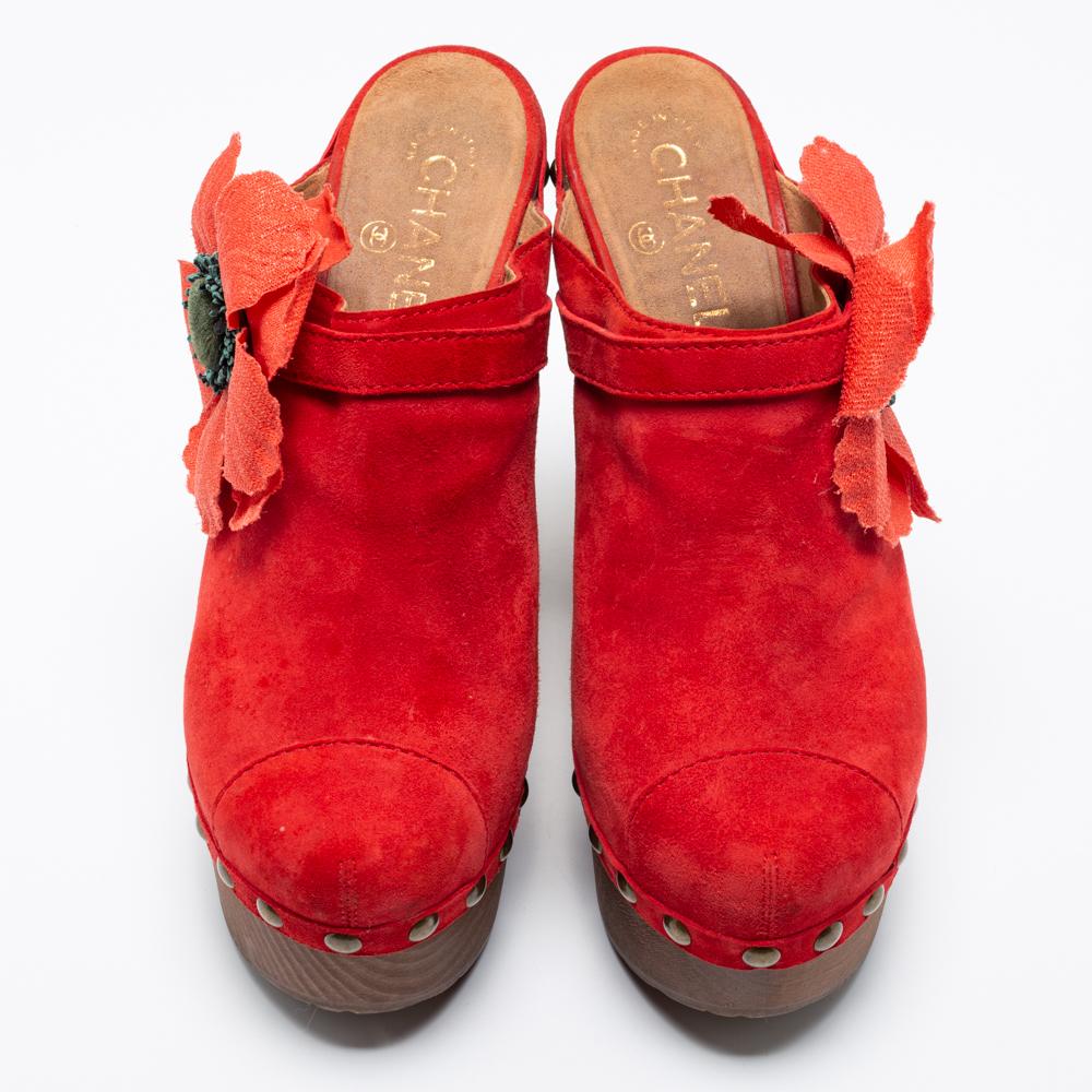 Imbued with stunning signatory elements and crafted into a beautiful silhouette, these clogs from Chanel are all you need to flaunt elegance! A Camellia motif decorates the red suede frame of these wooden clogs. Elevated on 16 cm block heels, these