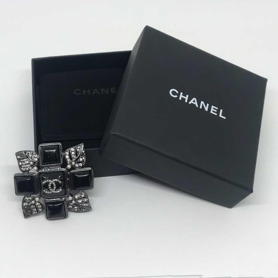 The jewel is from Maison CHANEL. A cross in black resin with the CC of the brand in its center. Each end of the cross has a leaf set with rhinestones and small pearls.
The brooch is in very good condition. No signs of wear. It is square with 5