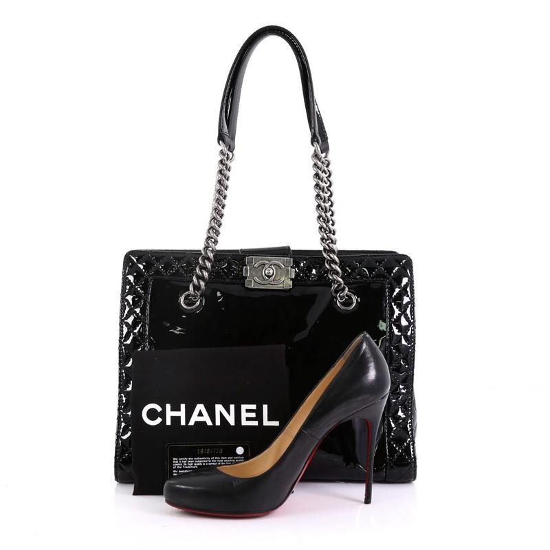 This Chanel Reverso Boy Chain Tote Patent Medium, crafted from black patent leather, features chain link straps with leather pads and aged silver-tone hardware. Its CC boy push-lock closure opens to a black fabric interior with zip and slip pockets.