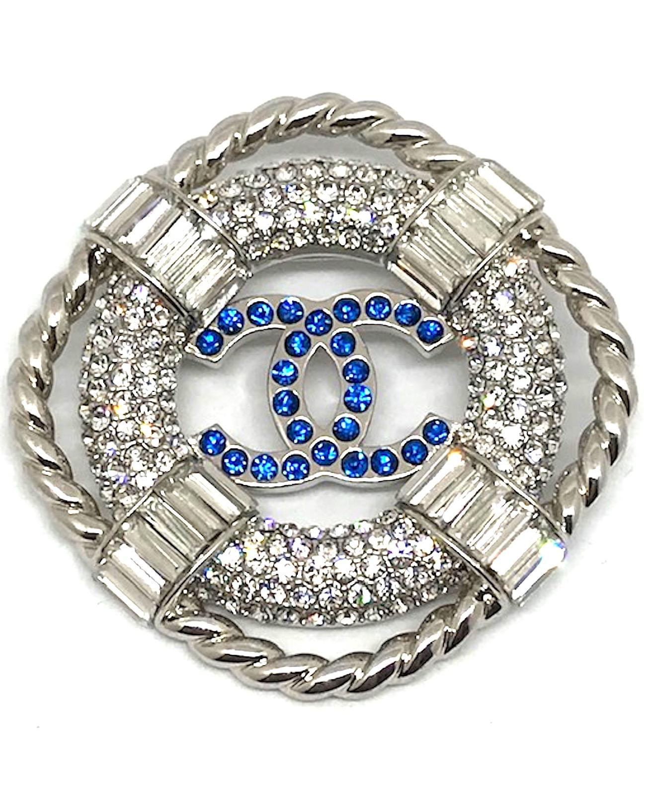 A lovely Chanel lifesaver nautical pin from the 2019 cruise collection. Rhodium plate set with pave' and baguette rhinestones. Blue rhinestone Chanel CC logo in the center of the lifesaver wheel and surrounded by a braided rope. On the back of the