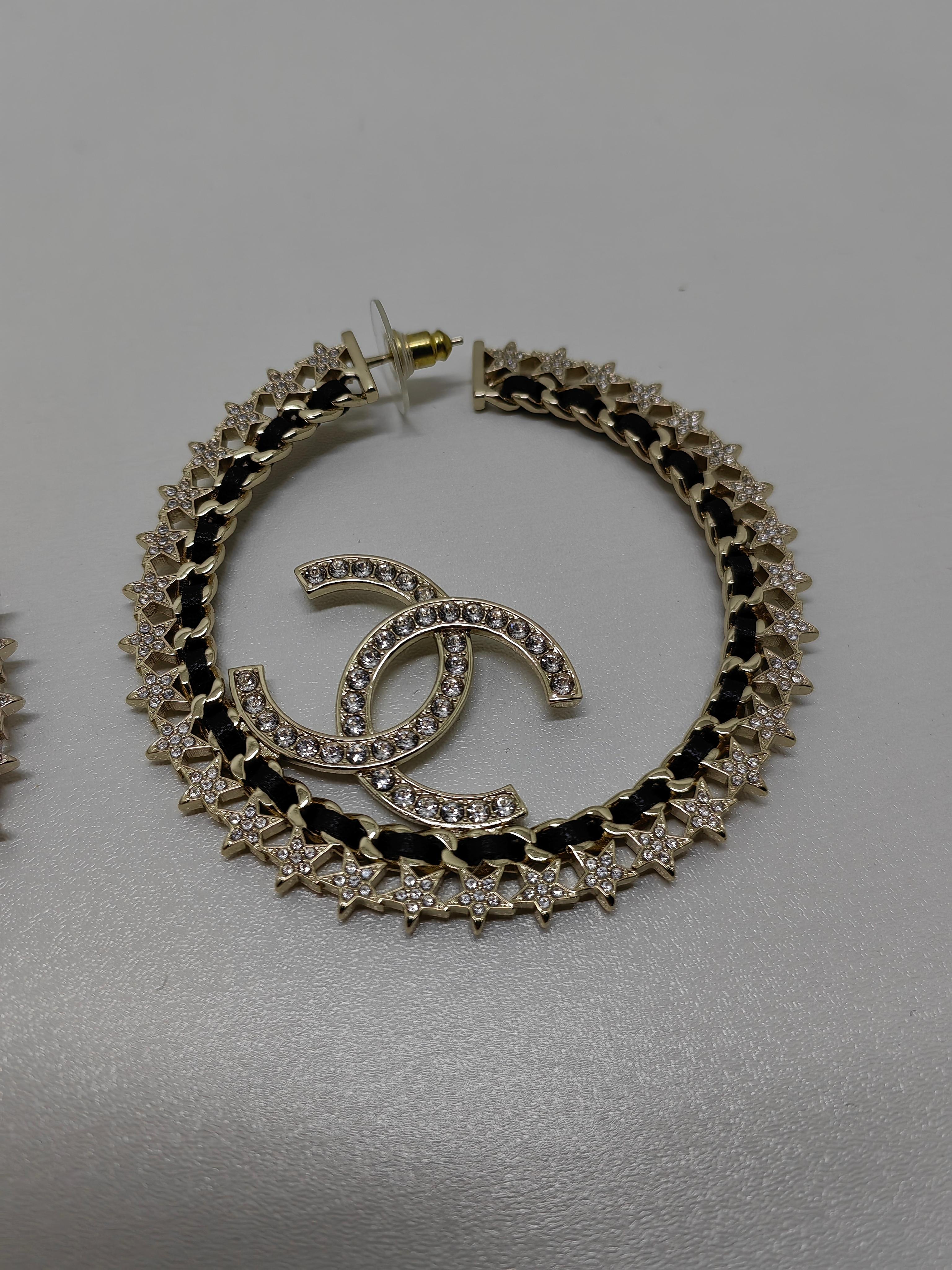 These dazzling Chanel hoop earrings combine modern elegance with the brand's iconic design aesthetic. Made with a polished silver-tone metal finish, they feature star-shaped details and shimmering rhinestones that add a touch of celestial glamour.