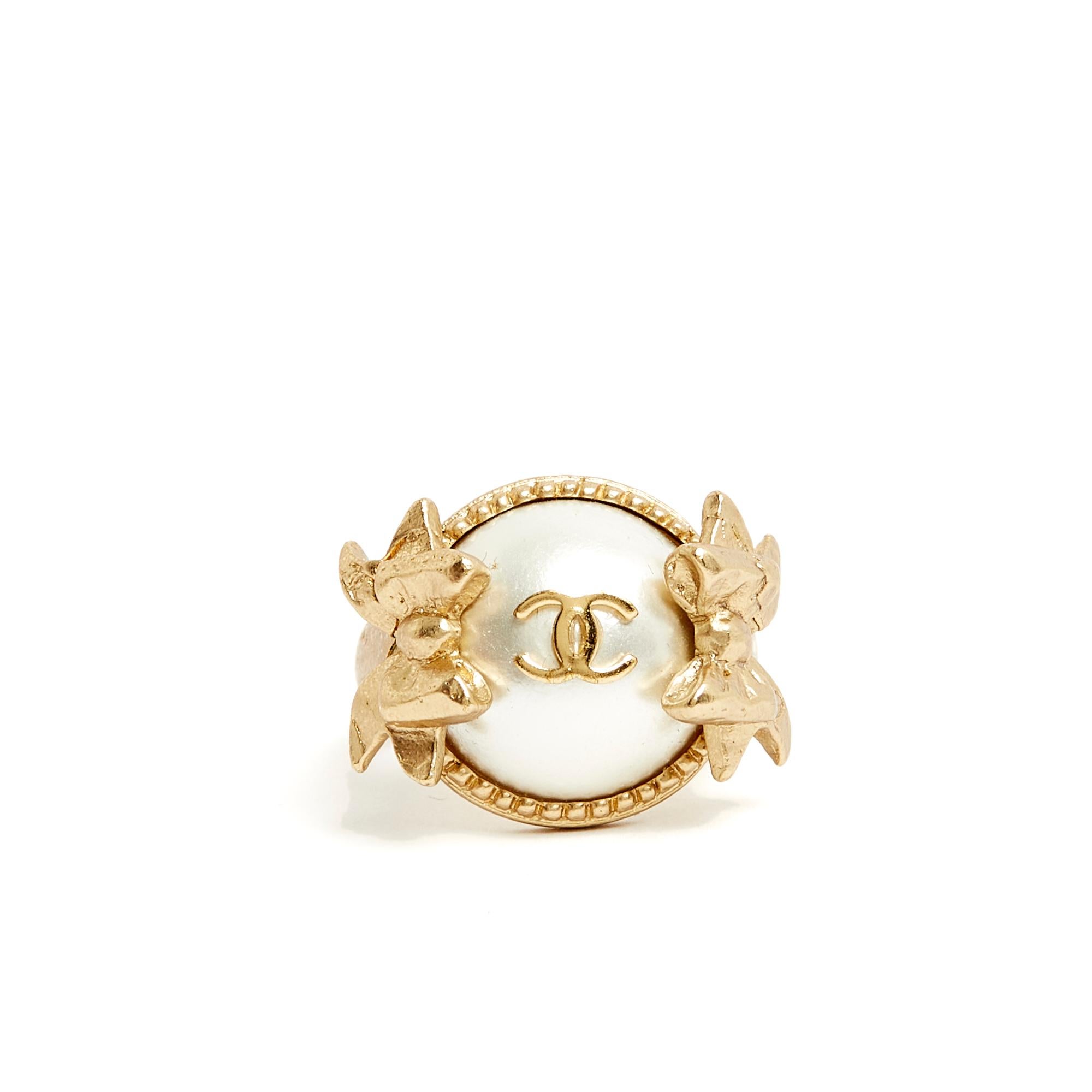 Chanel ring in matte gold metal with a ring topped with a half fancy pearl surrounded by 2 ribbons and topped with a CC symbol. Finger size 54/55 mm or US7.25, diameter 1.75 cm, total height of the ring 2.8 cm. The ring is delivered without invoice