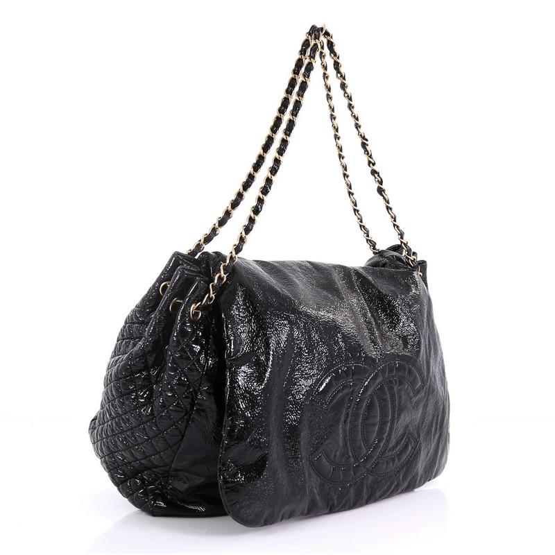 This Chanel Rock and Chain Flap Bag Patent XL, crafted in black patent leather, features woven-in leather chain straps, large CC stitched design on its front flap, diamond quilted side panels, and gold-tone hardware. Its hidden snap closure opens to