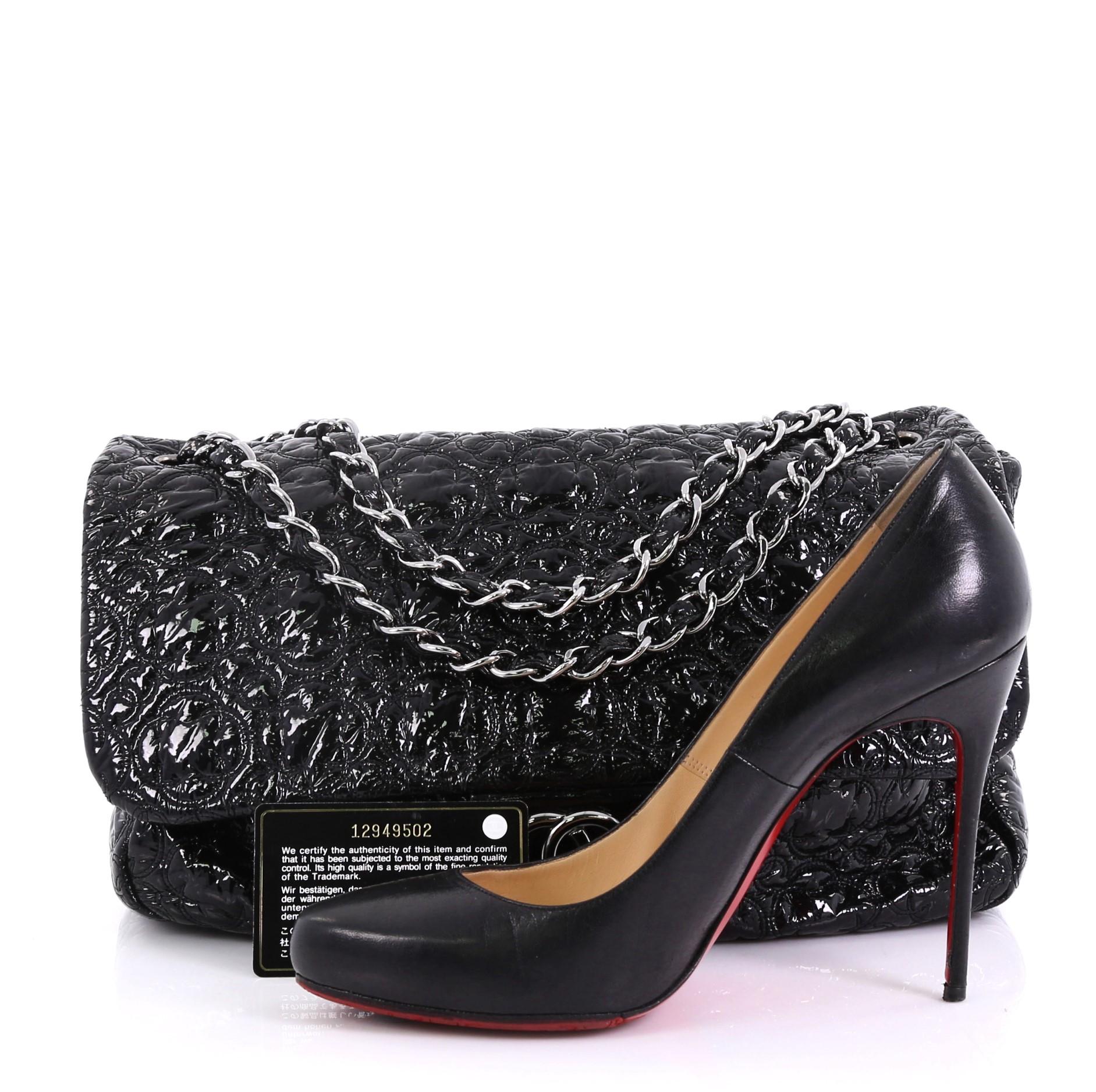 This Chanel Rock In Moscow Flap Bag Patent Vinyl Jumbo, crafted from black patent vinyl, features dual woven-in vinyl chain straps, quilted CC logo and geometric patterns, and silver-tone hardware. Its magnetic snap button closure opens to a gray
