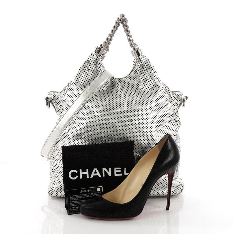 This Chanel Rodeo Drive Hobo Perforated Leather Large, crafted in metallic silver perforated leather, features dual chain link handles, detachable leather strap, and silver-tone hardware. Its magnetic snap closure opens to a gray satin interior with