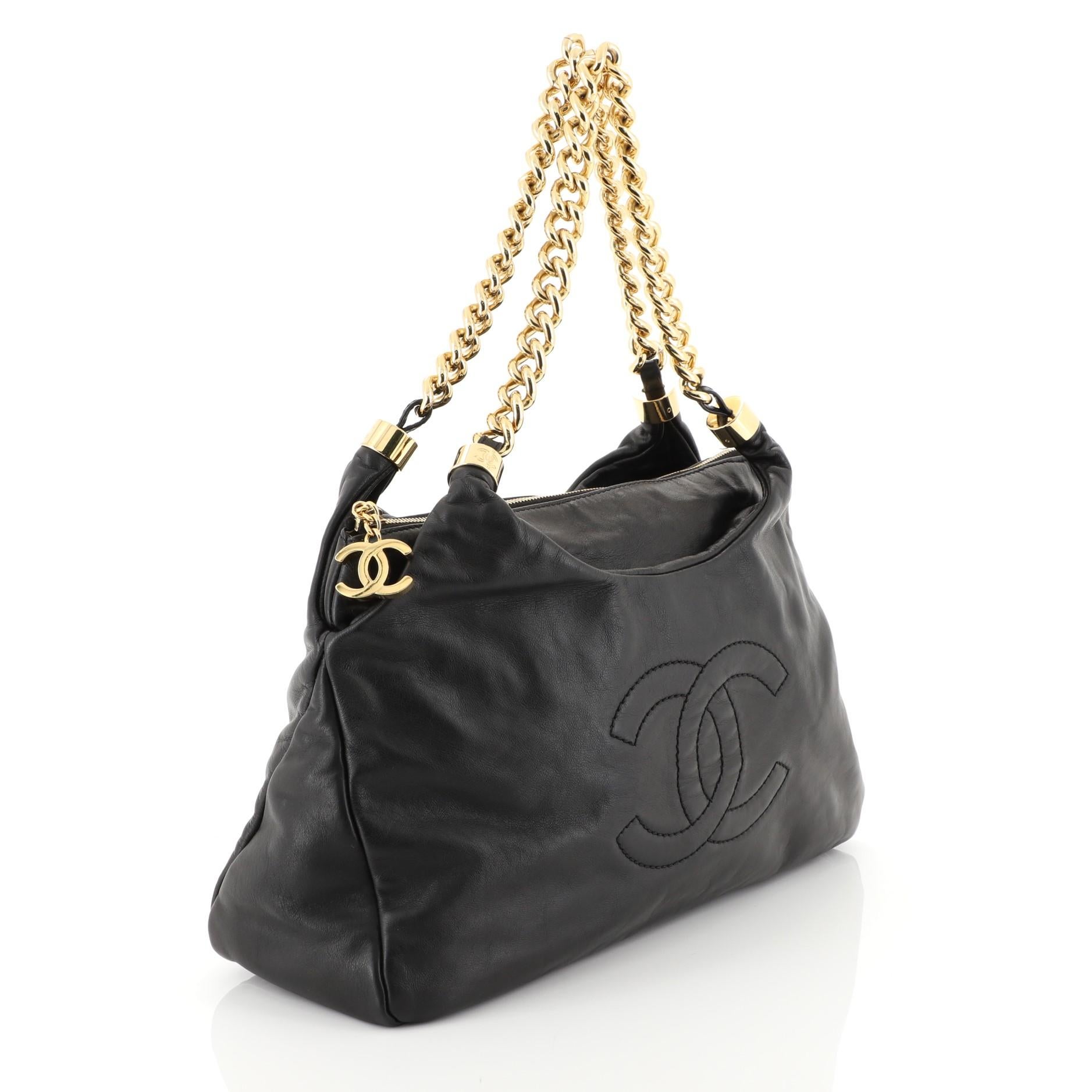 This Chanel Rodeo Drive Zip Hobo Lambskin Small, crafted from black lambskin, features dual chain link straps, interlocking CC stitched logo at front, CC charm zip pull, and gold-tone hardware. Its zip closure opens to a neutral satin interior with