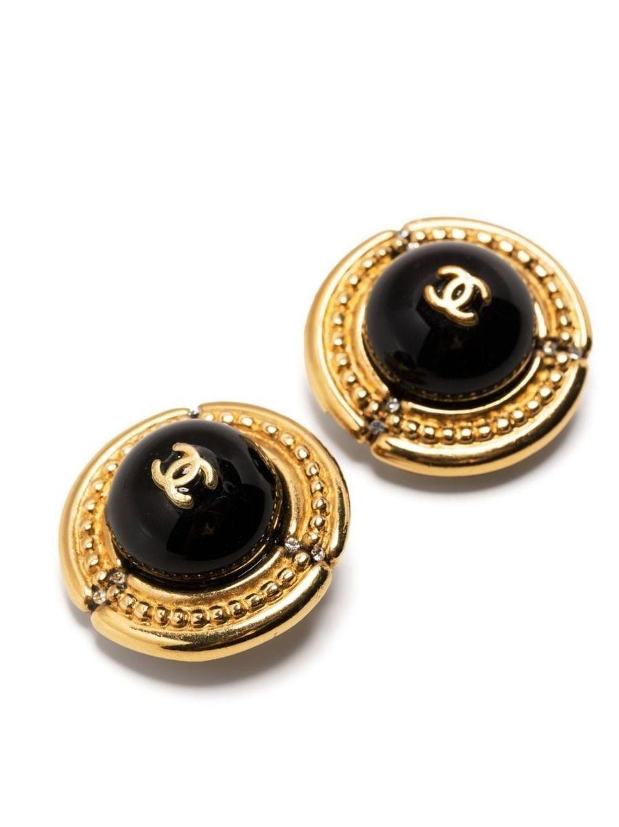 Designed with a large black cabochon set against a gold-toned base, these vintage Chanel earrings feature a beaded detailing embossed into the base, alongside small glimmering rhinestones. Displaying the brand's signature CC logo in the centre,
