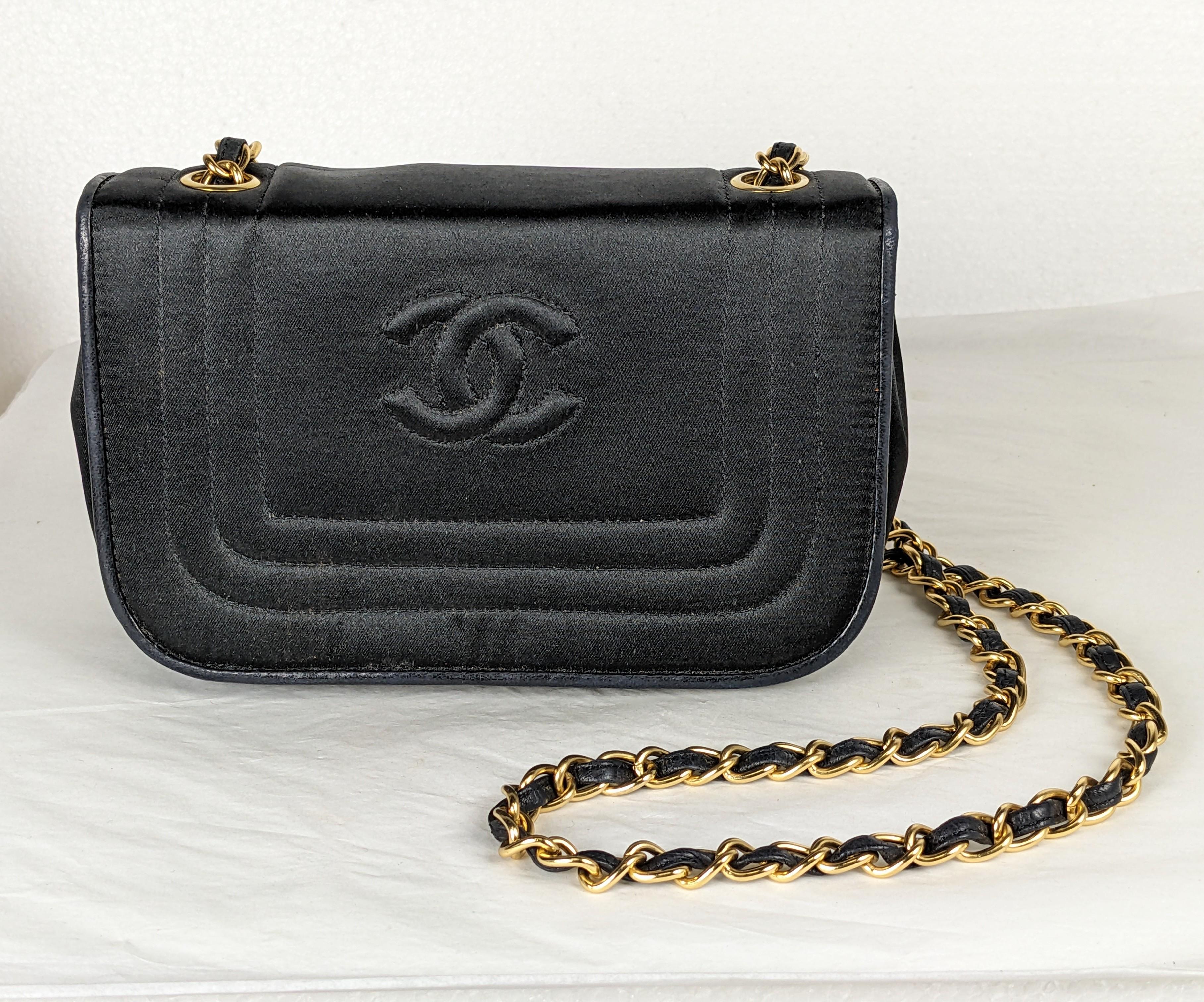 Timeless and Chic Chanel Satin and Calfskin Mini Shoulder Bag circa 1990's. Black silk satin quilted and logo'd with leather piping and lining. One zip interior pocket. Long leather and gilt bronze crossbody chain strap. Authentic Chanel bag,