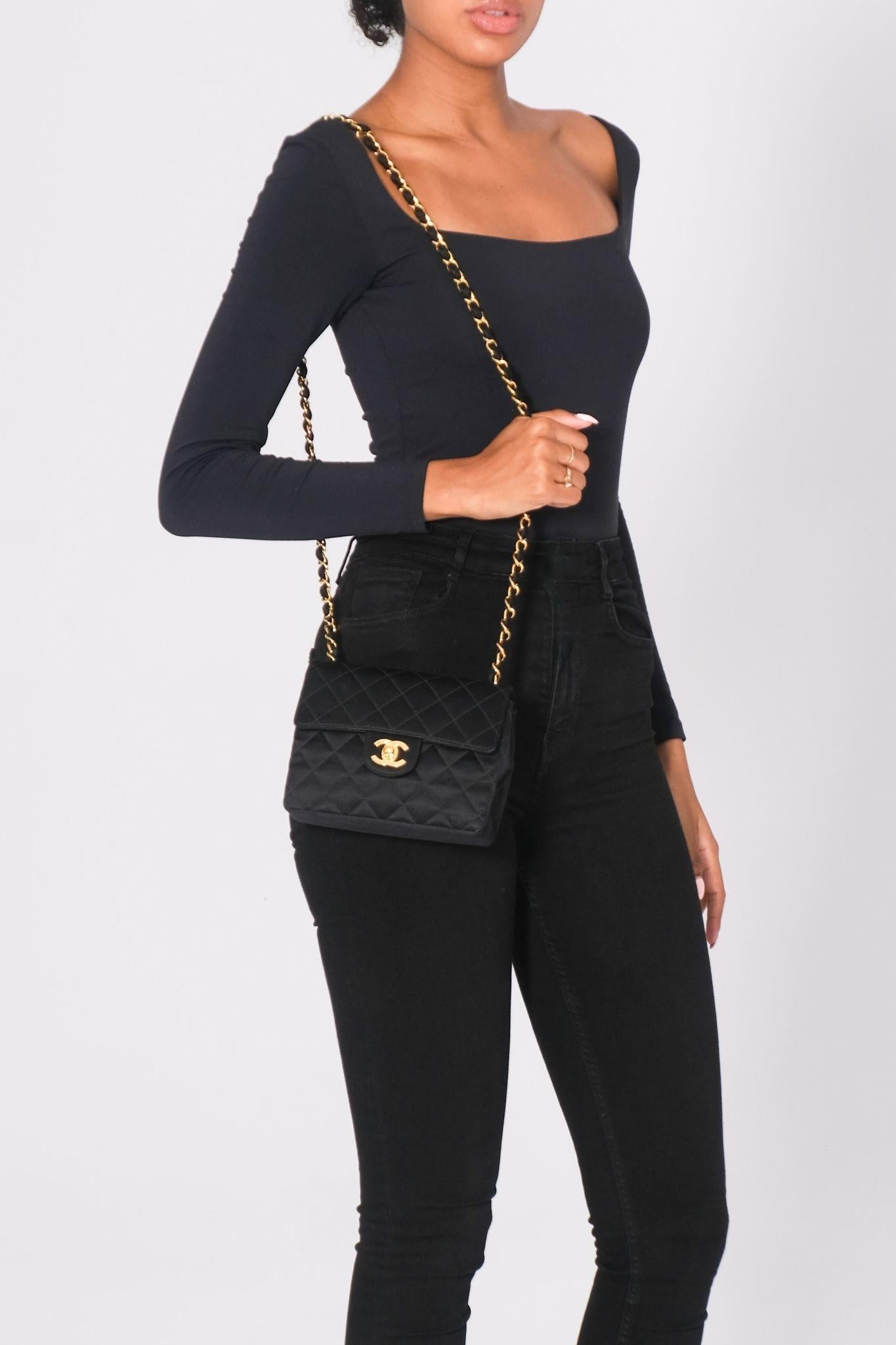 This classic Chanel mini square flap bag is constructed of black satin with gold hardware. It features a front flap, a back slip pocket, signature interlocking CC turn-lock closure, and diamond quilting. The long chain and leather shoulder strap