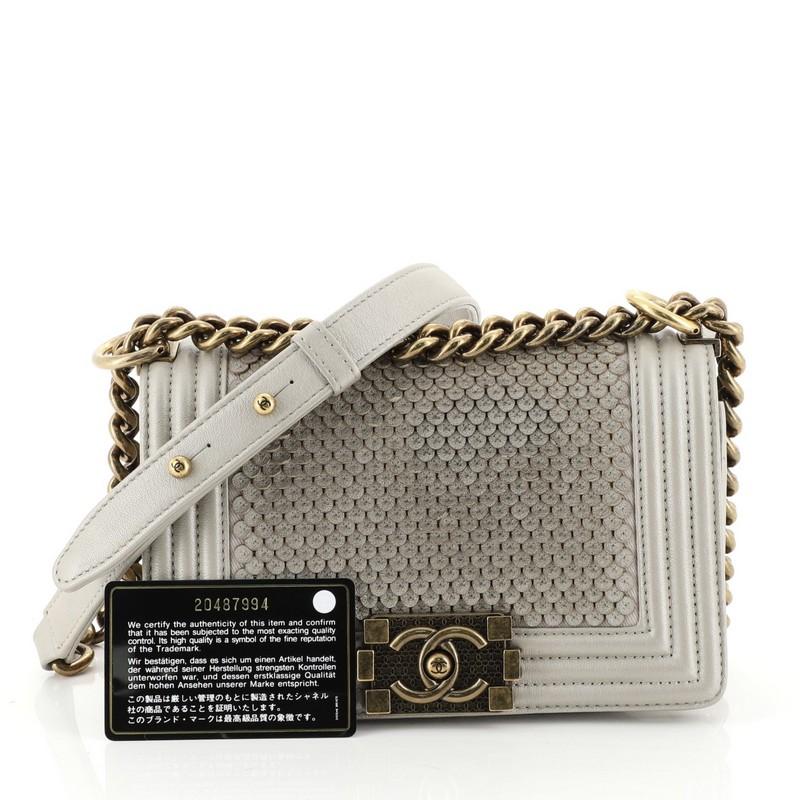 This Chanel Scaled Boy Flap Bag Lambskin Small, crafted from neutral metallic lambskin leather, features a chunky chain link strap with shoulder pad, laser cut lambskin scales, and aged gold-tone hardware. Its CC Boy logo push-lock closure opens to